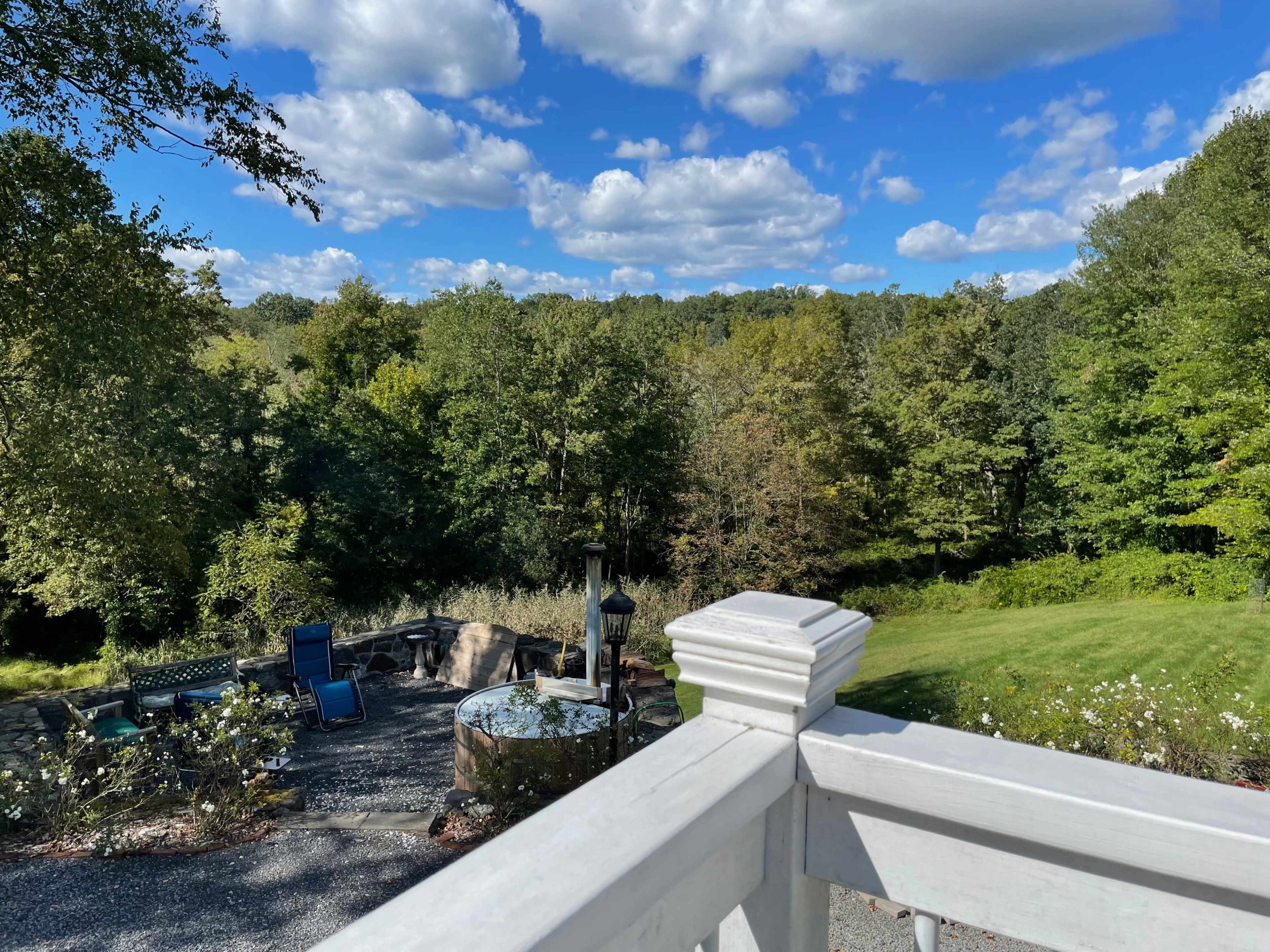 A view from a white railing overlooks a landscaped backyard with seating areas and trees under a partly cloudy sky.