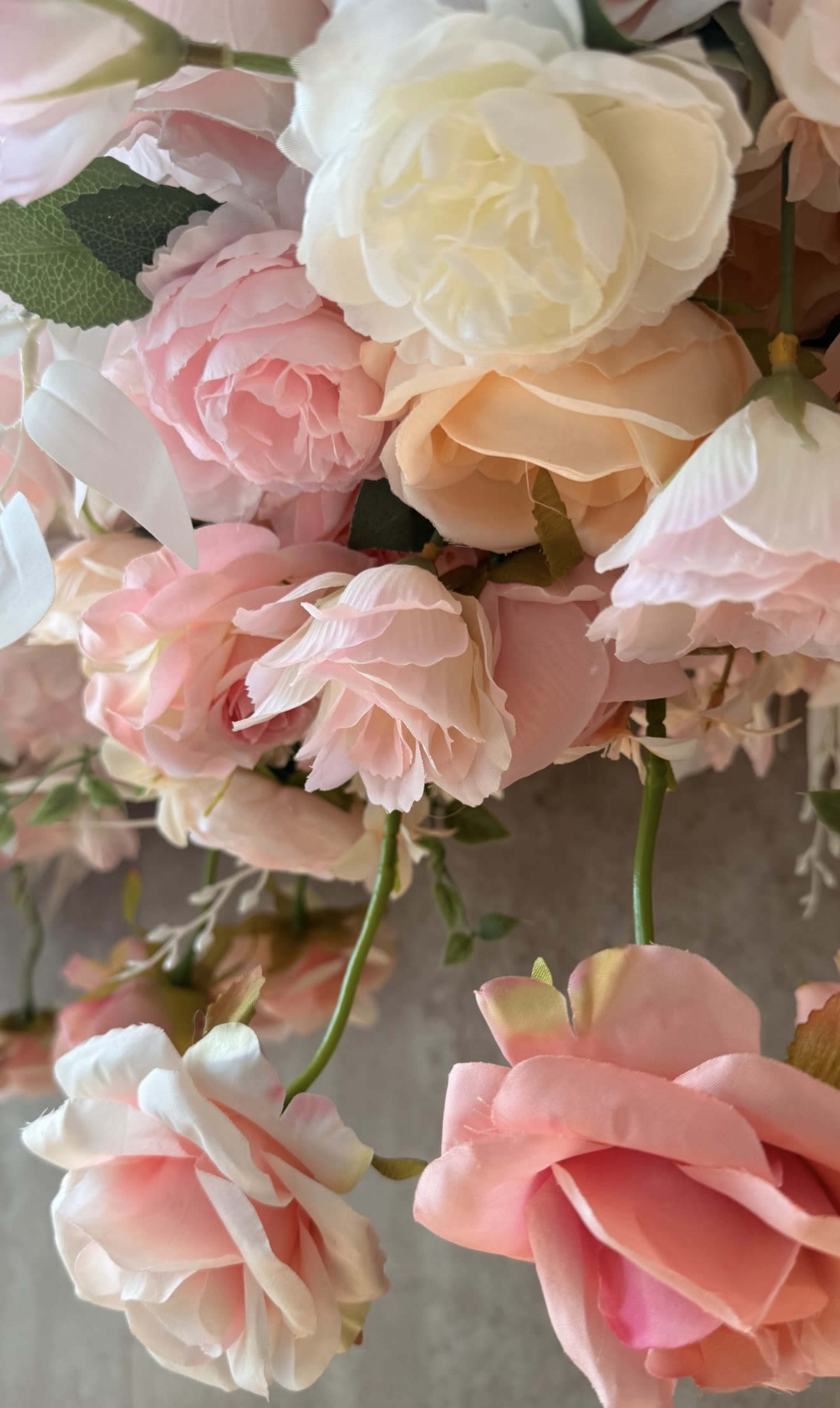 The image features a close-up view of artificial roses in various shades of pink and cream, arranged with green leaves.
