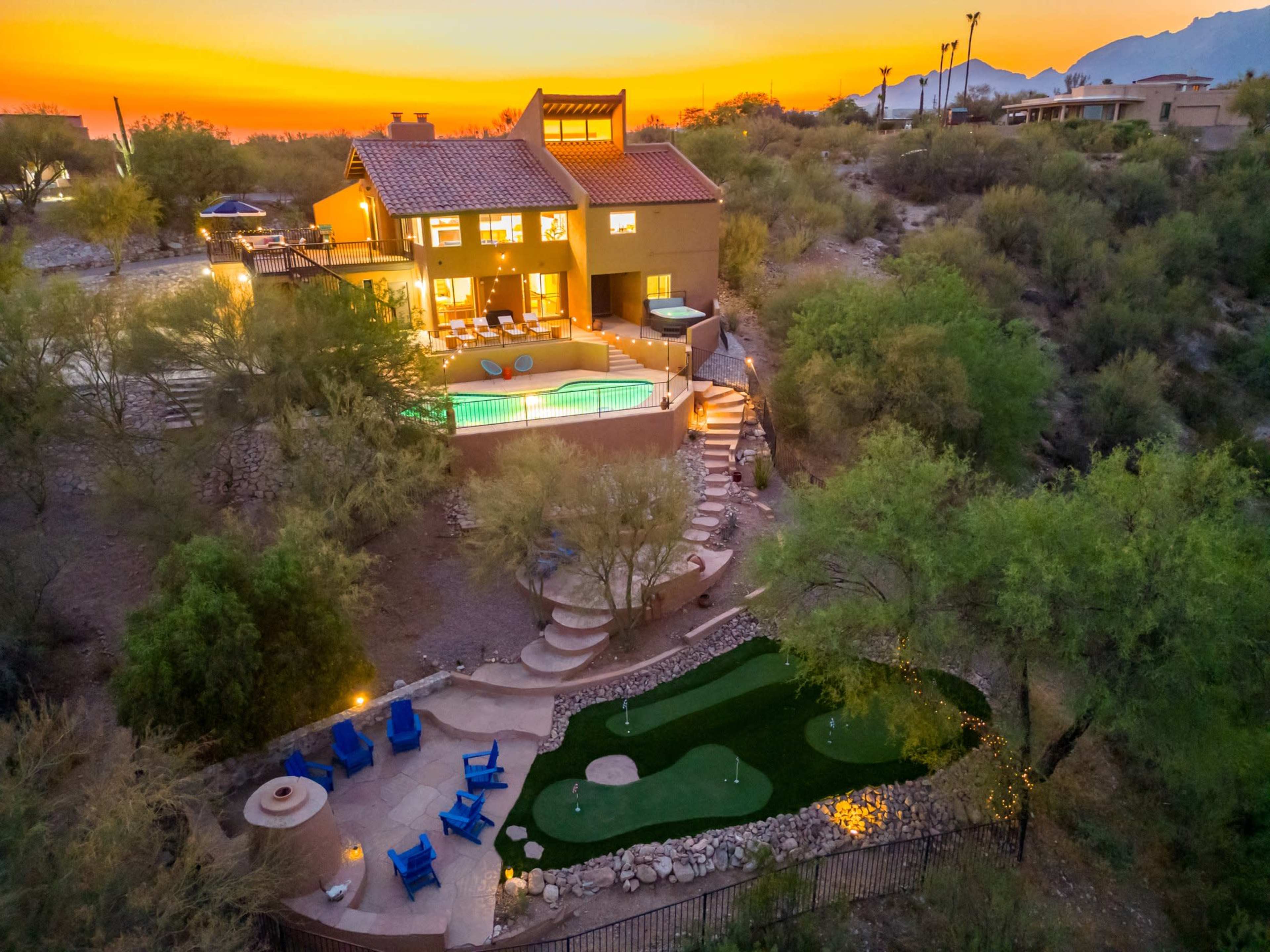 A hillside home with a swimming pool and a putting green surrounded by desert vegetation at sunset.