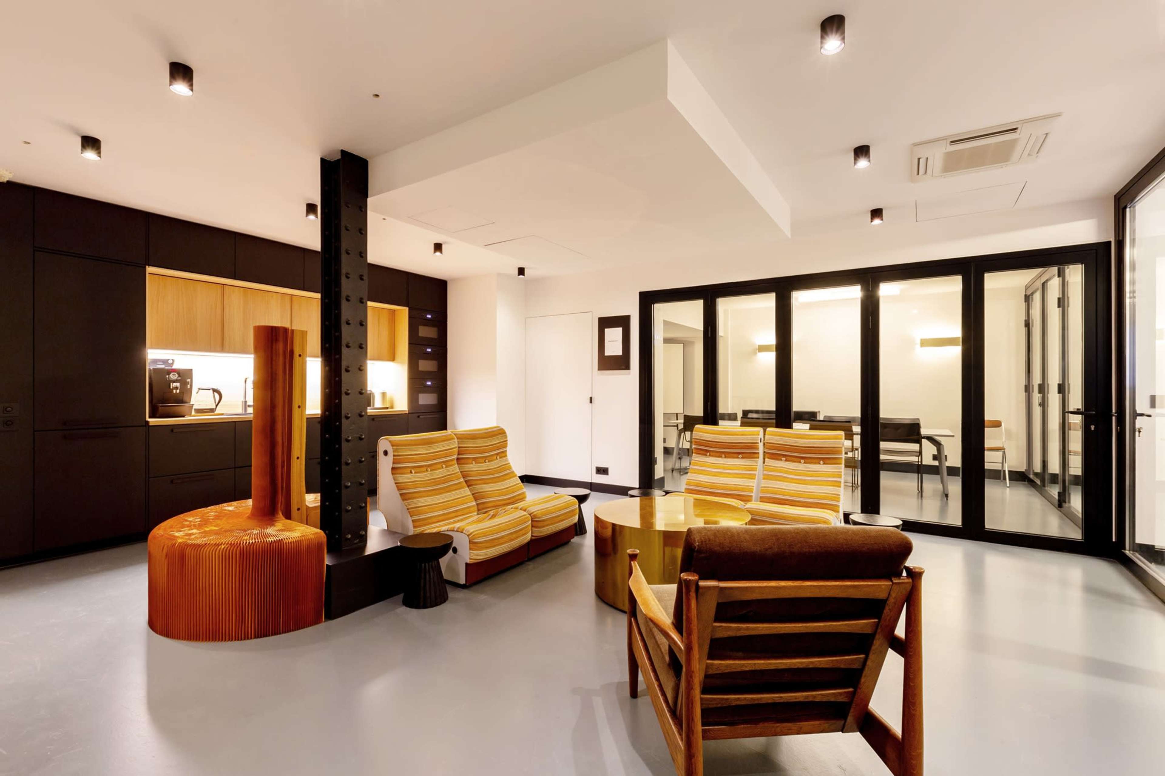 The image shows a modern interior space featuring two striped armchairs, a wooden table, and a glass-walled meeting room.