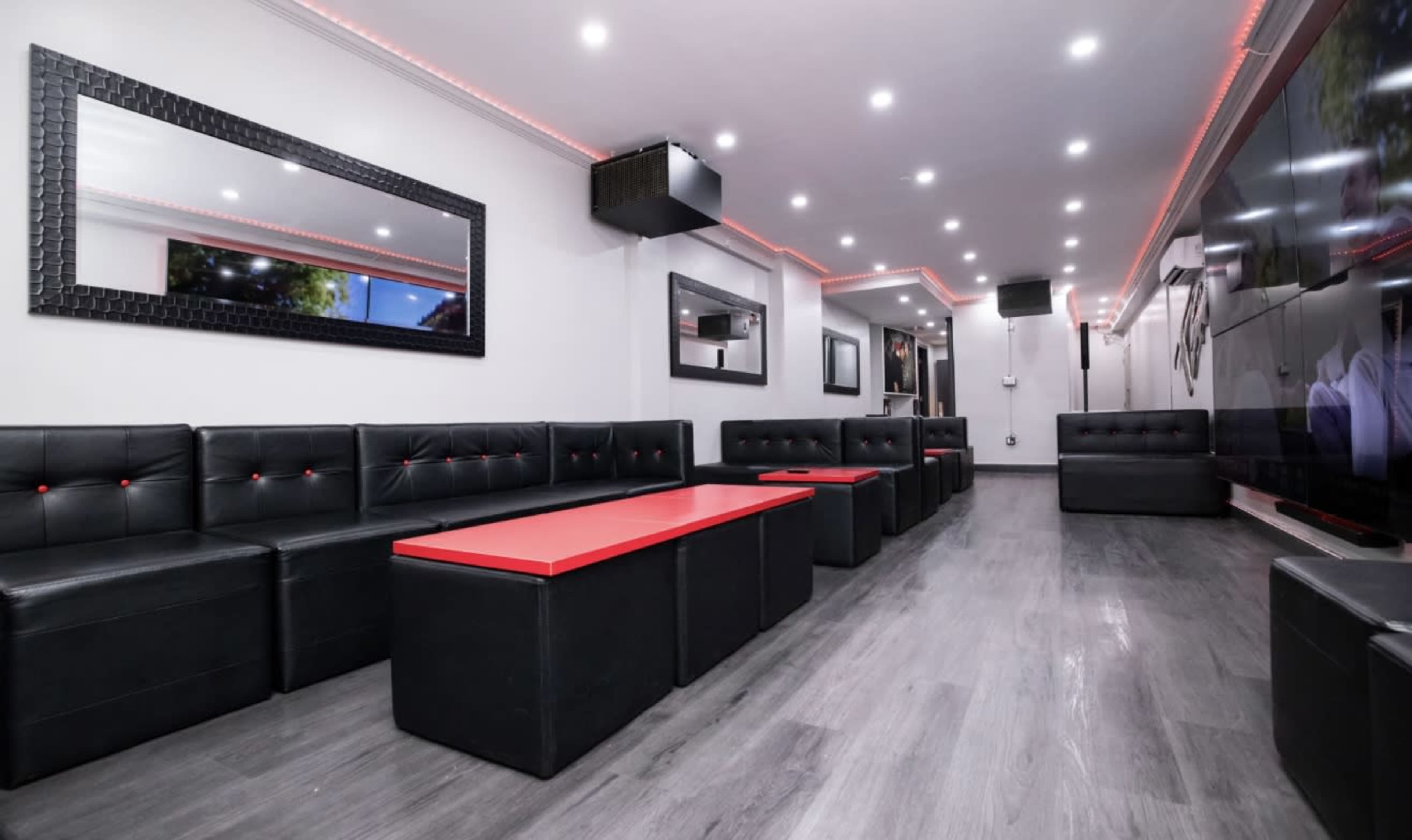 The image shows a modern interior of a lounge with black leather seating, a red table in the center, and ambient lighting.