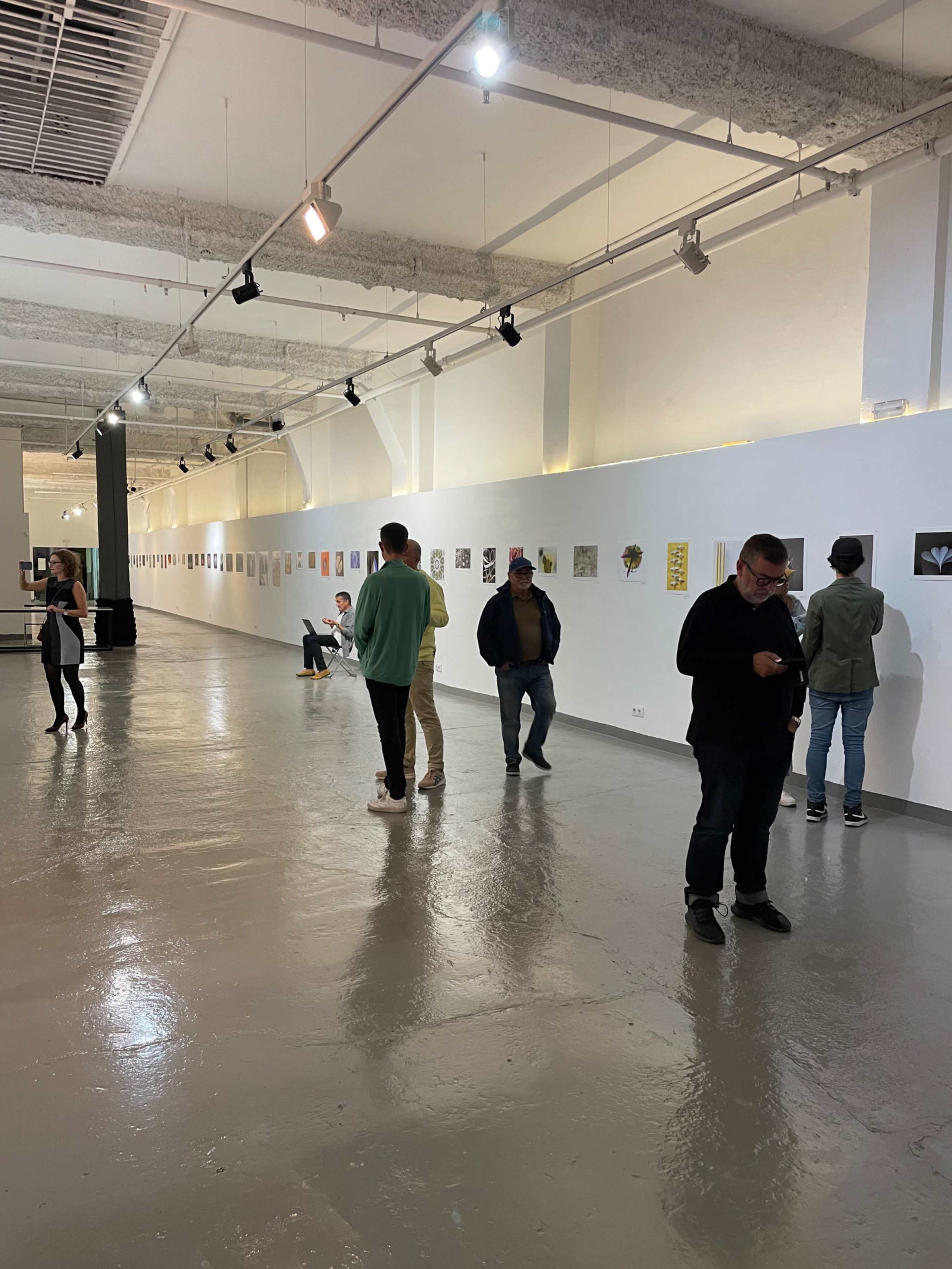 An art gallery with several people examining artworks displayed on the walls in a spacious, well-lit area.