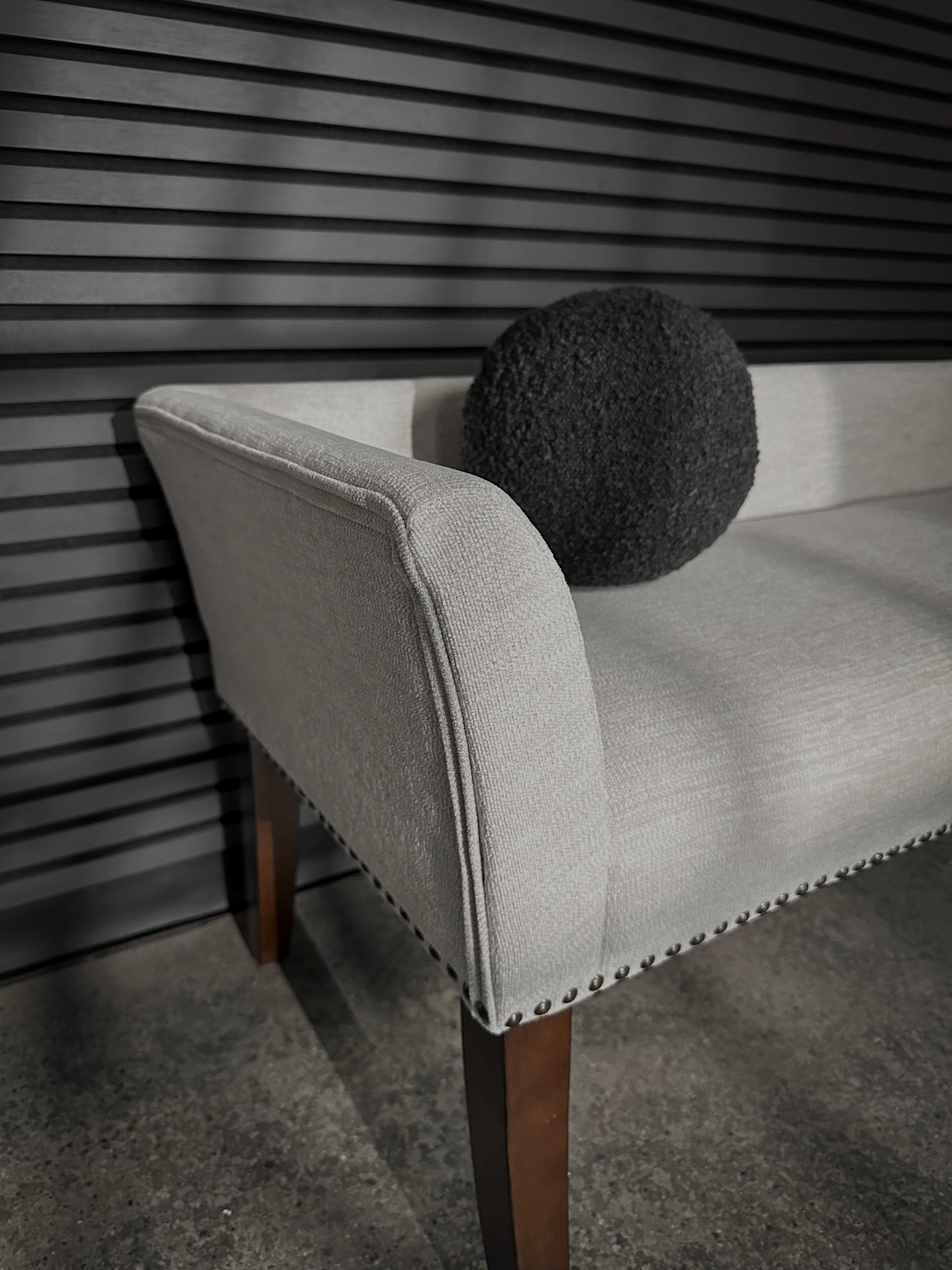 A light-colored sofa with a rounded black cushion rests against a striped dark wall.