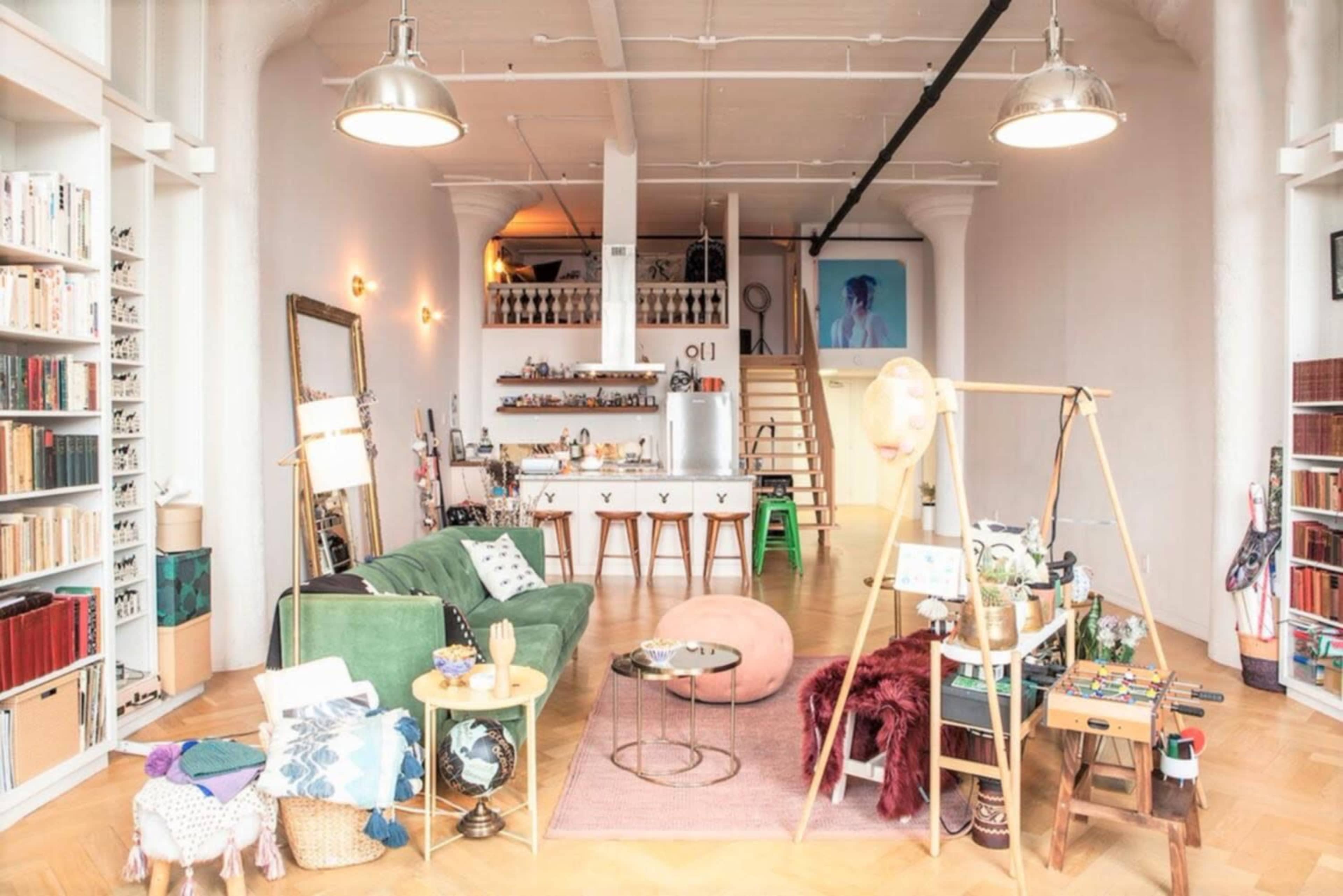 A spacious living room with a green sofa, a large bookshelf, an art piece on the wall, and an array of decor items, including a hanging wooden frame and a circular table.
