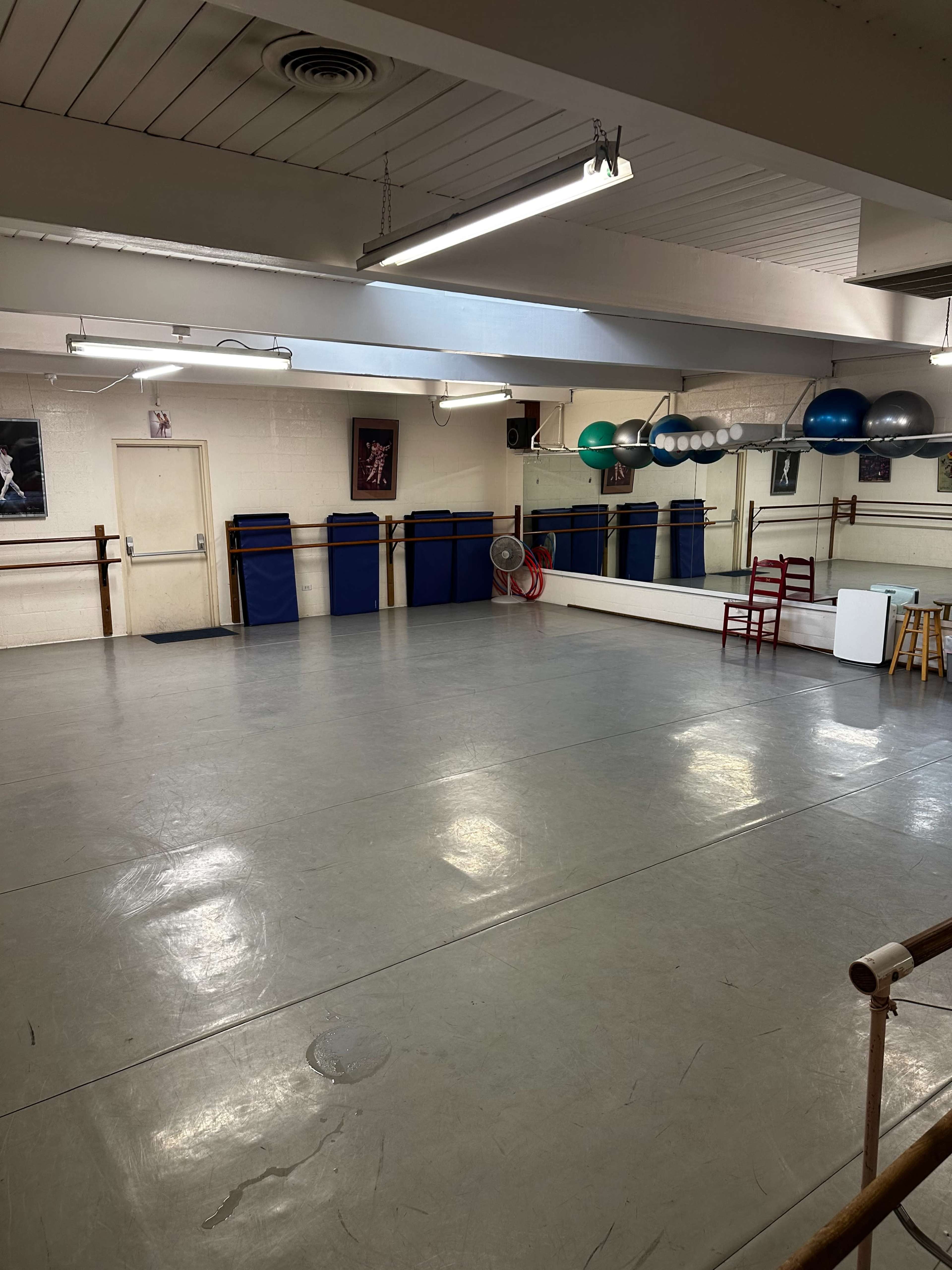 The image shows a spacious dance studio with mirrored walls, exercise balls, and wooden ballet barres.