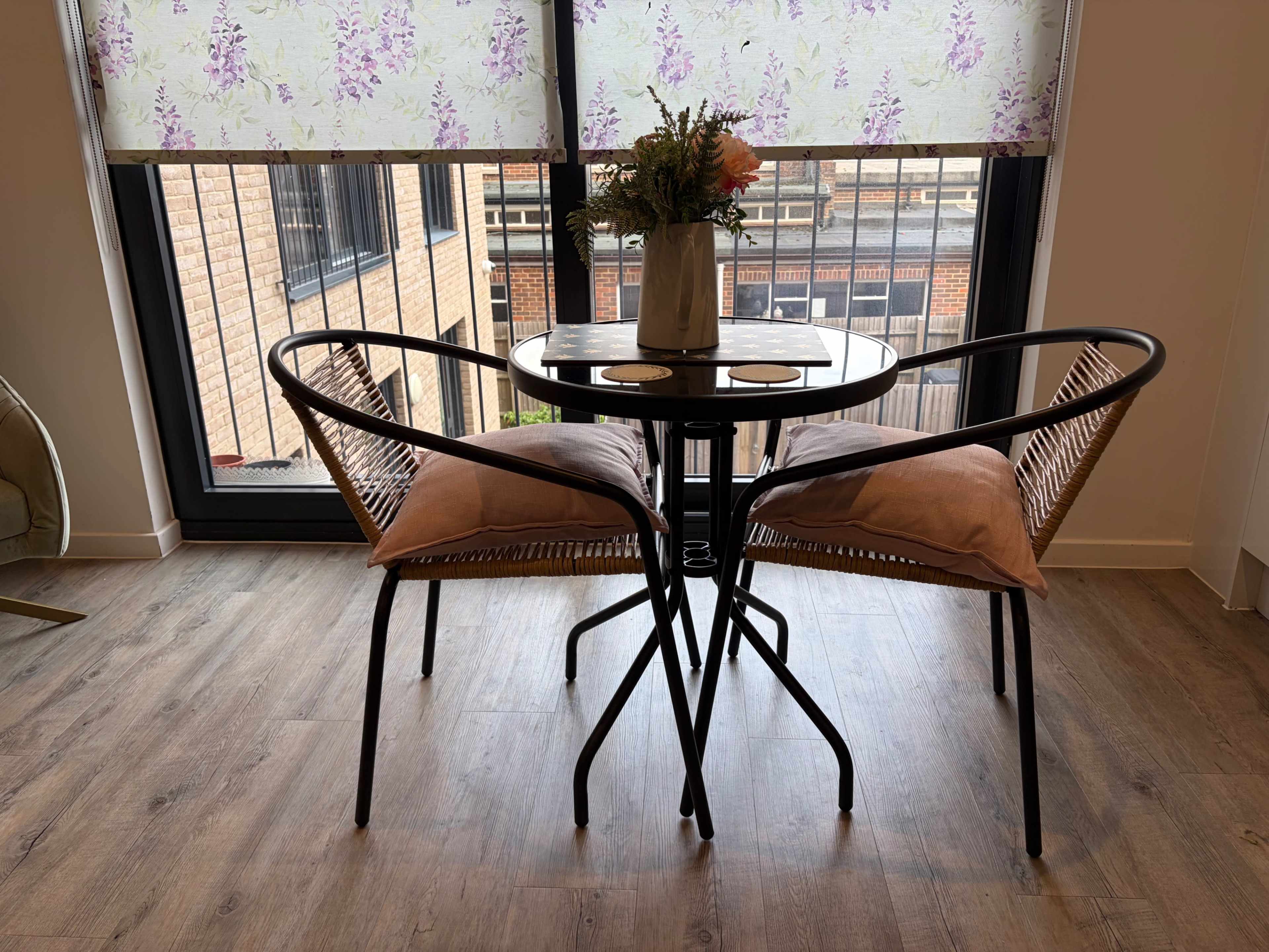 A small dining table with two chairs is positioned next to a window, featuring a vase of flowers on the table.