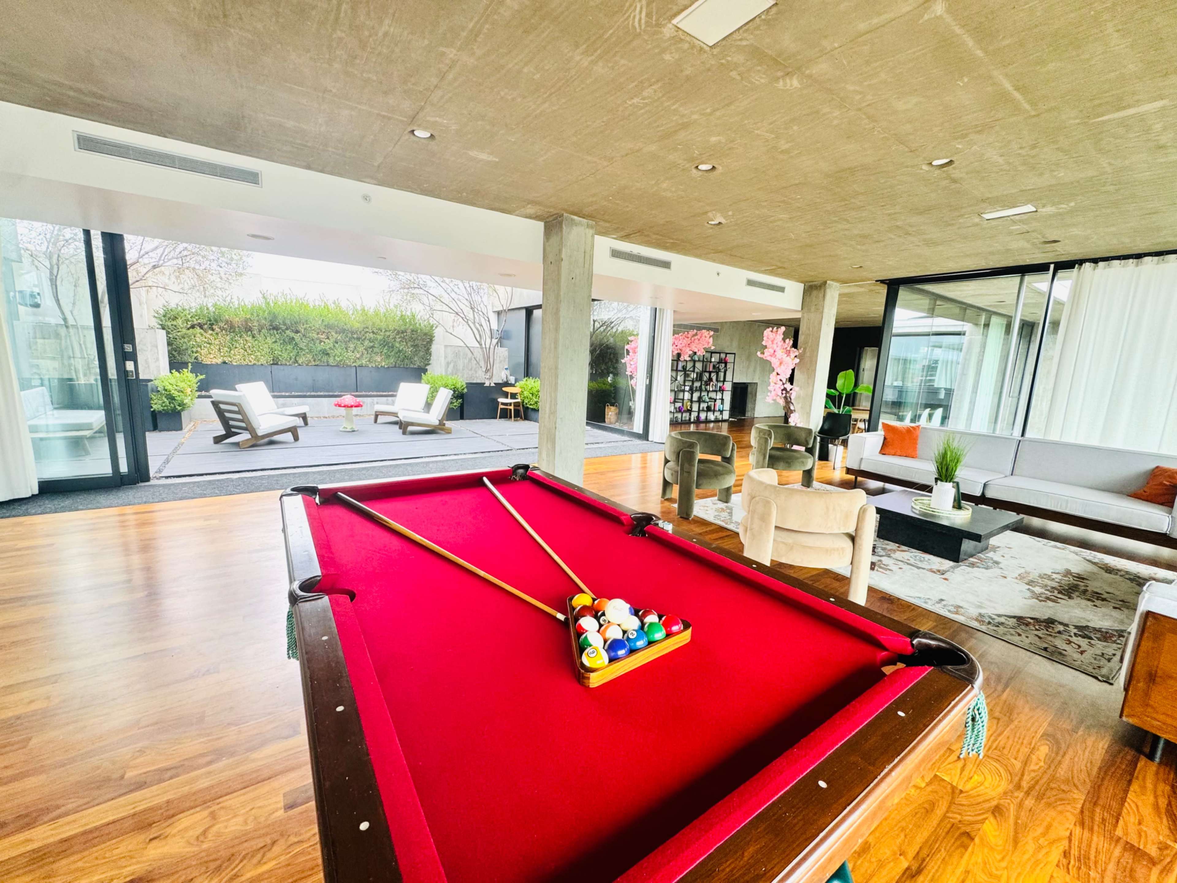 A pool table with a set of balls is centered in a modern living space that features large windows and stylish furniture.