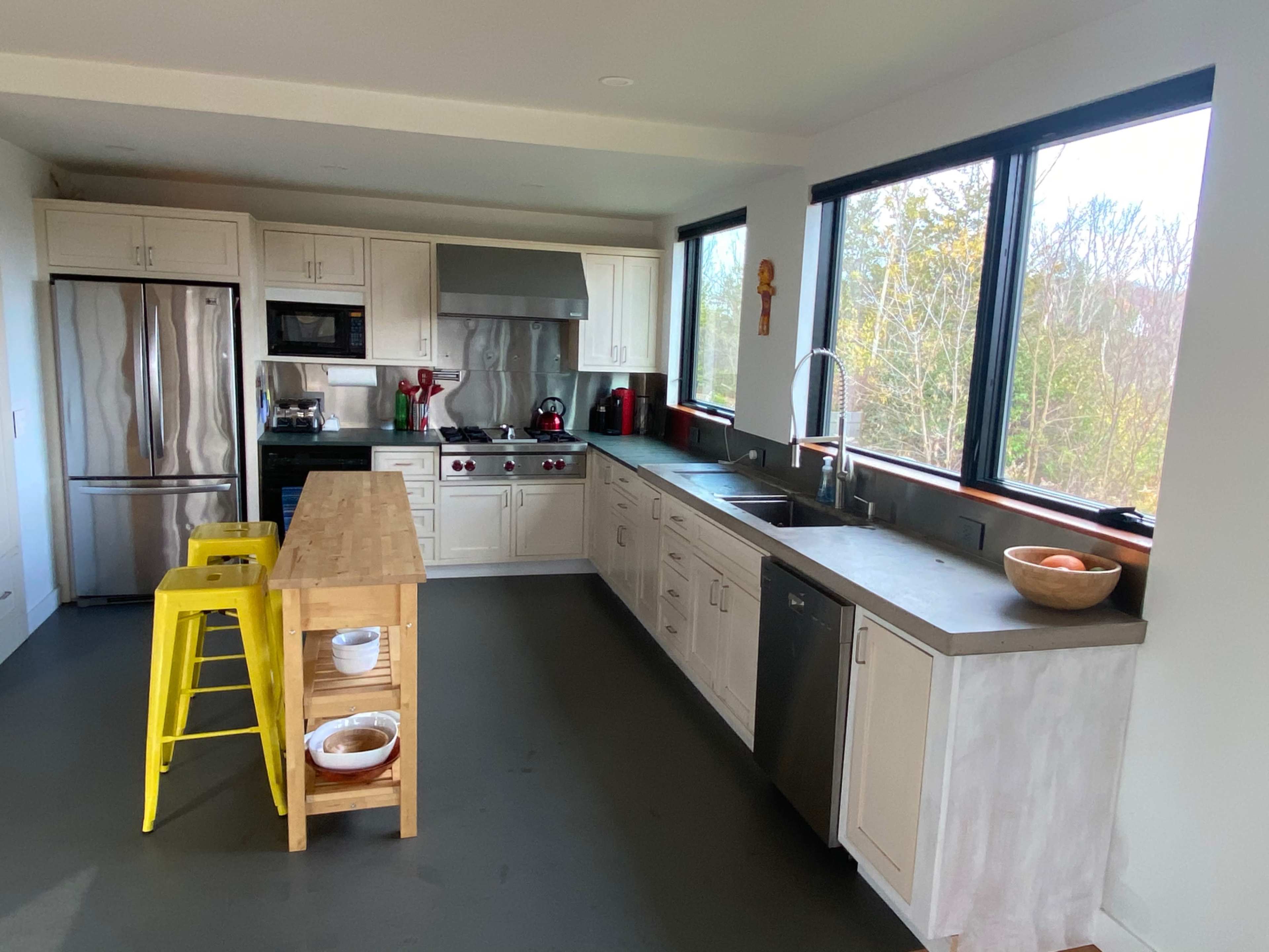 A modern kitchen with stainless steel appliances, a central wooden island, and large windows facing a view of trees.