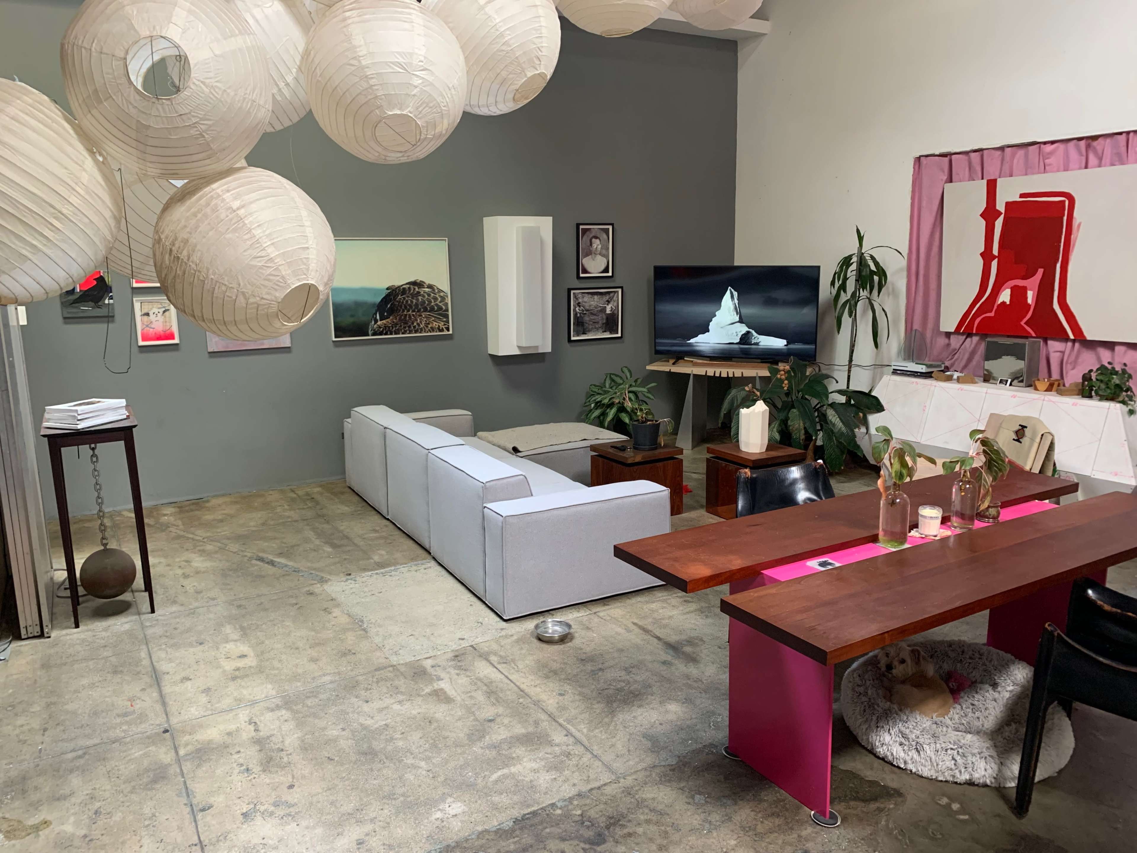 The image shows a modern living room featuring a white sectional sofa, a wooden dining table, and decorative paper lanterns hanging from the ceiling.