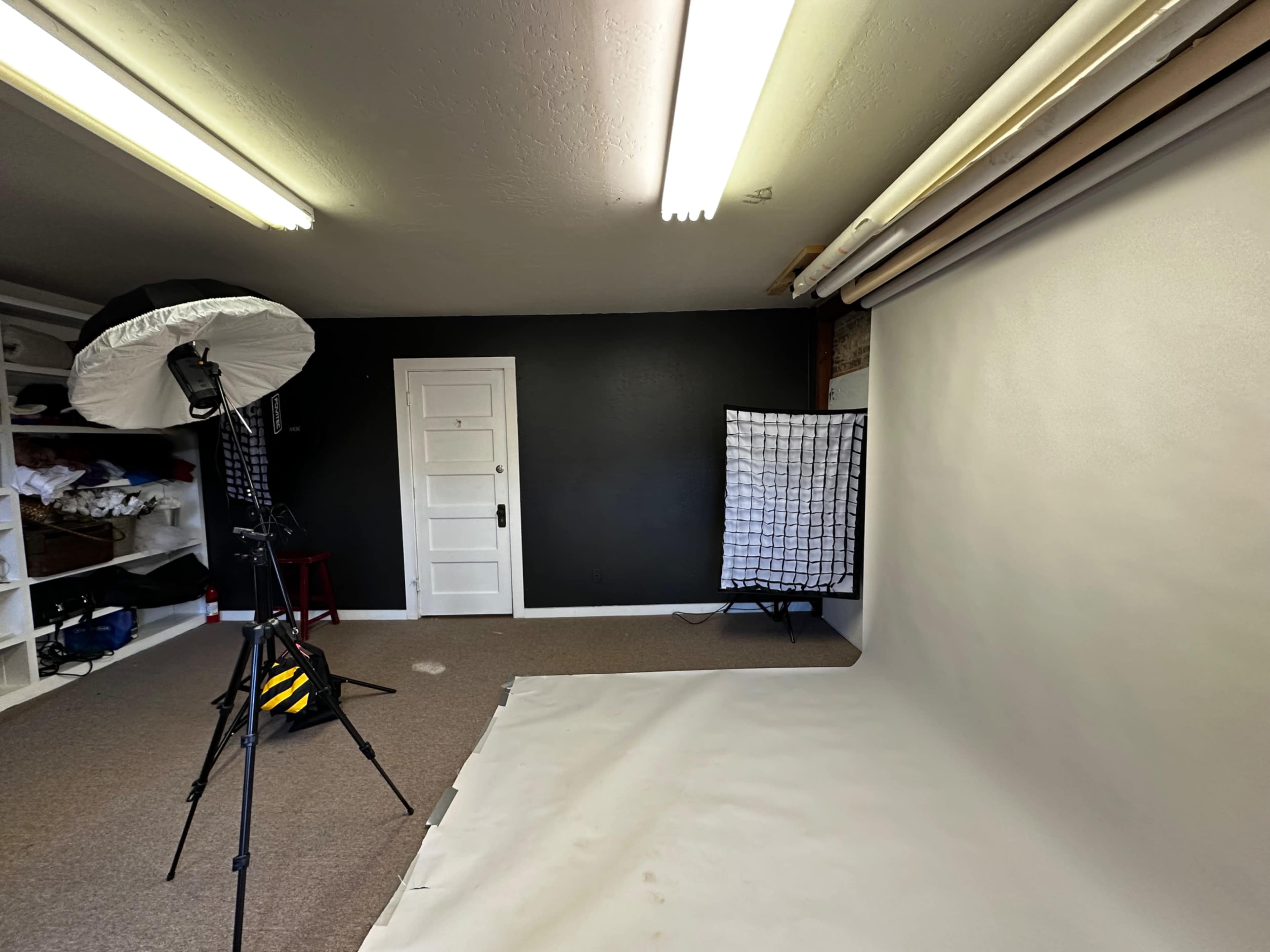 A photography studio features a seamless white backdrop, lighting equipment, and shelves filled with materials.