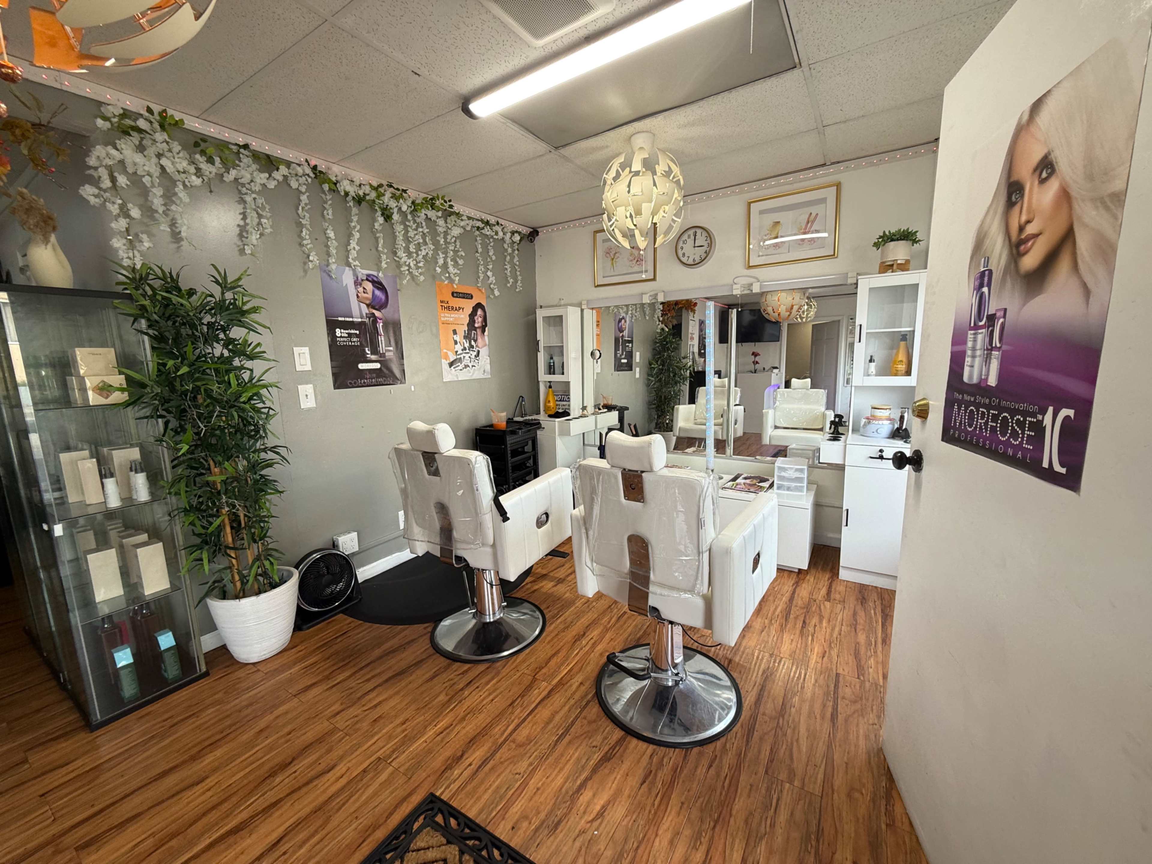 The image shows a bright, modern salon interior featuring two styling chairs, a mirrored vanity area, and product displays.