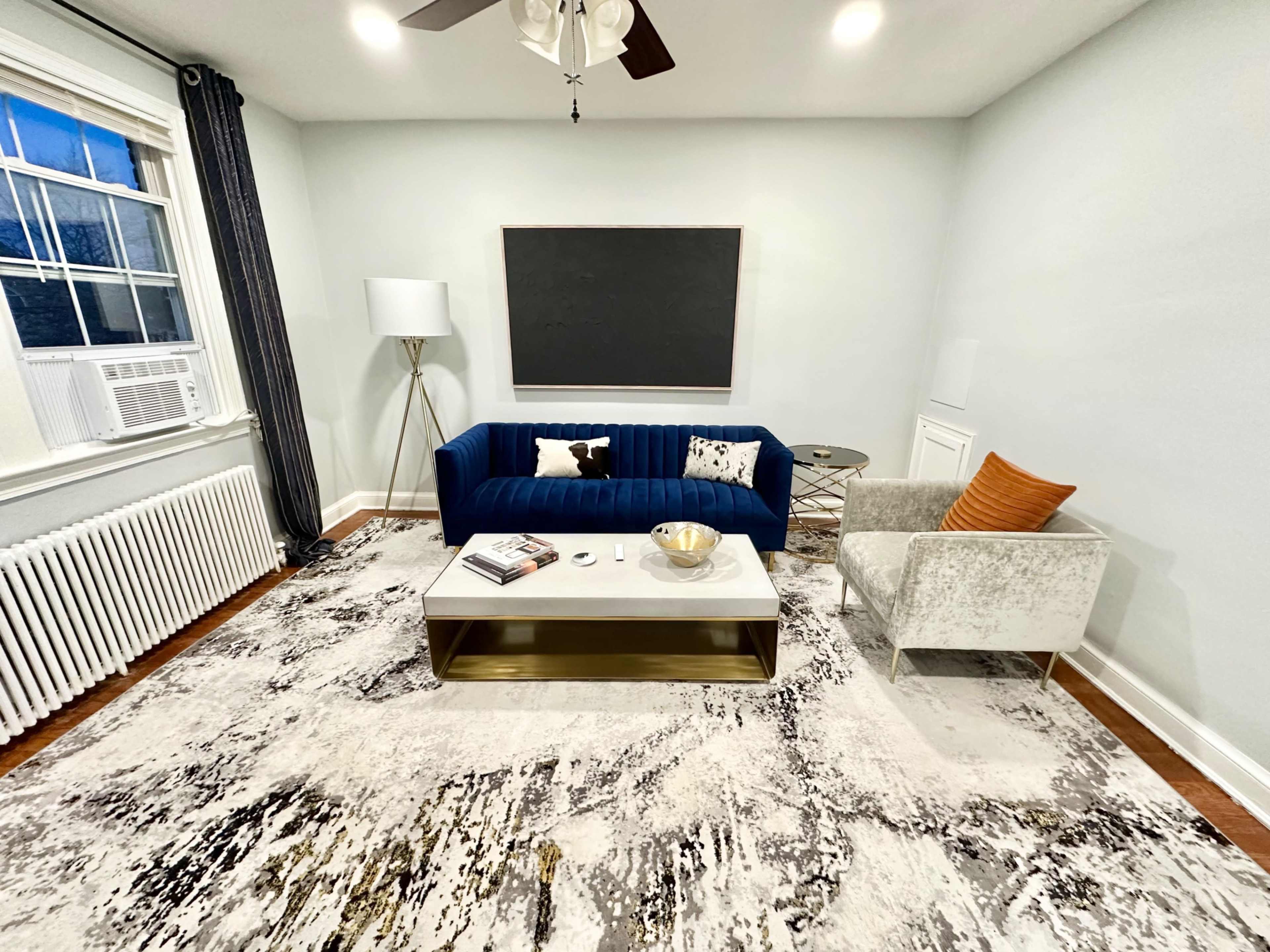 A living room with a blue velvet sofa, a white coffee table with a gold base, and a patterned area rug.