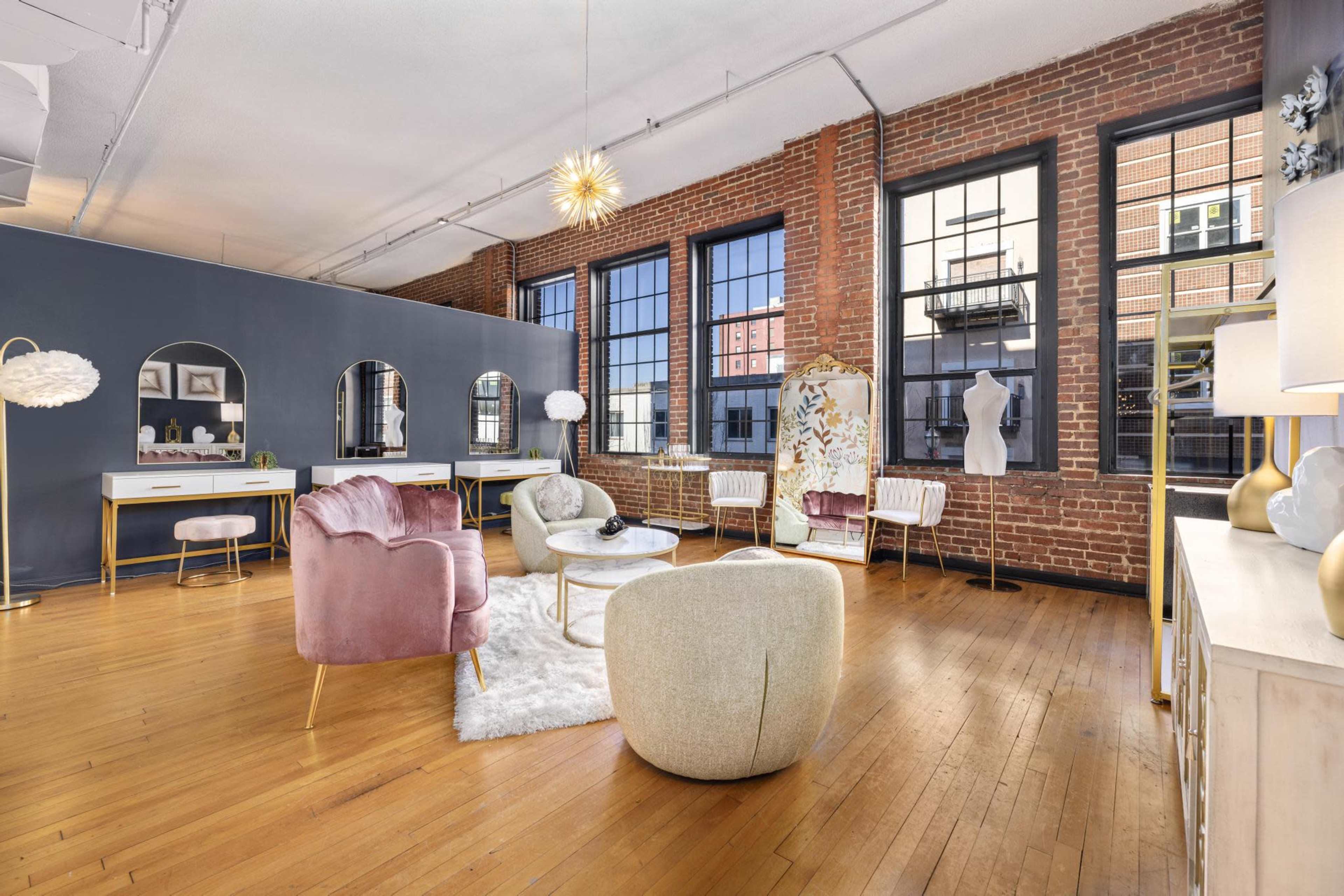 A stylish interior space with wooden floors, exposed brick walls, and modern furniture arranged around a central area featuring a white rug.