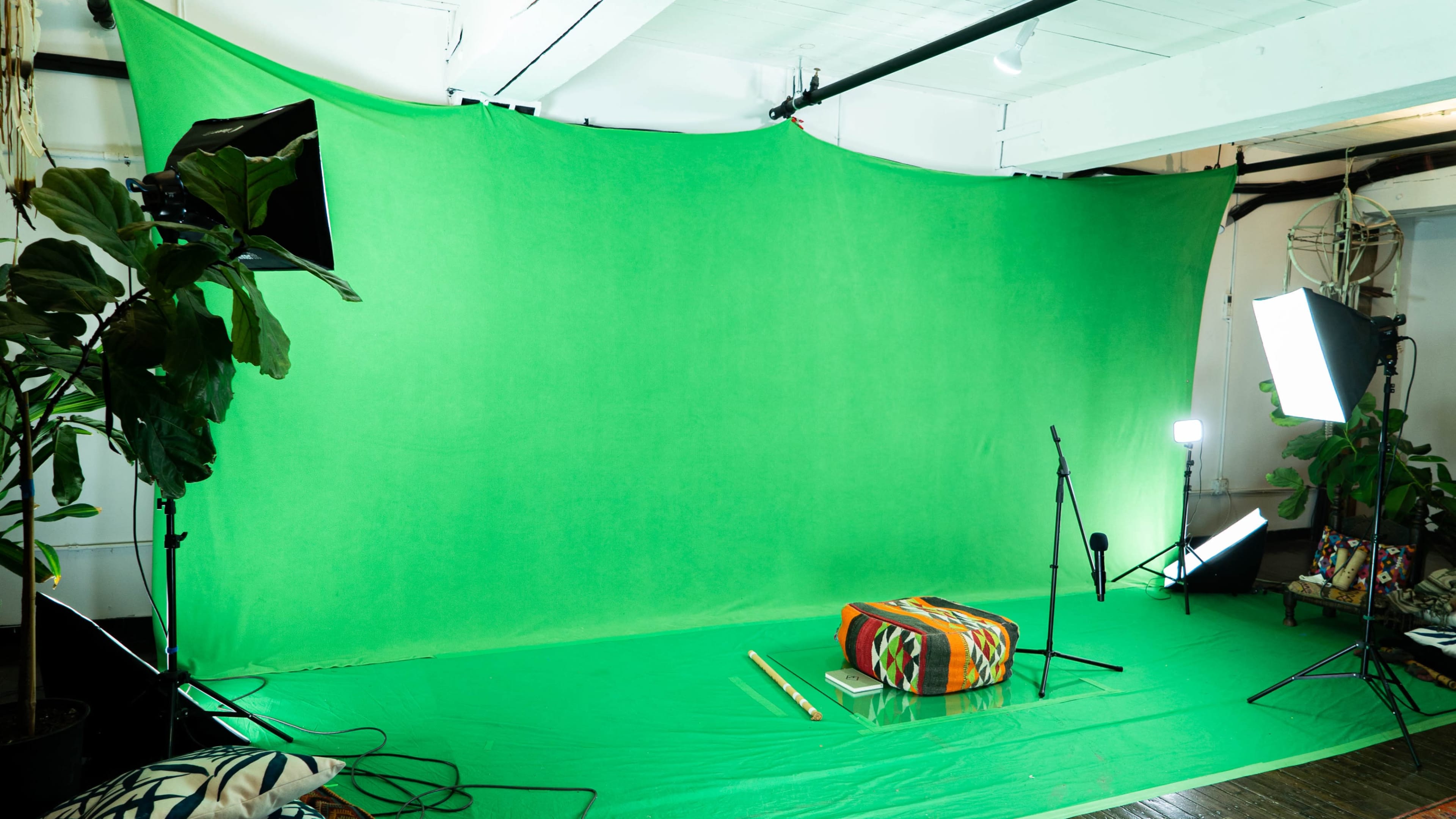 A green screen backdrop set up in a spacious room, with various lighting equipment and a colorful drum positioned in front.