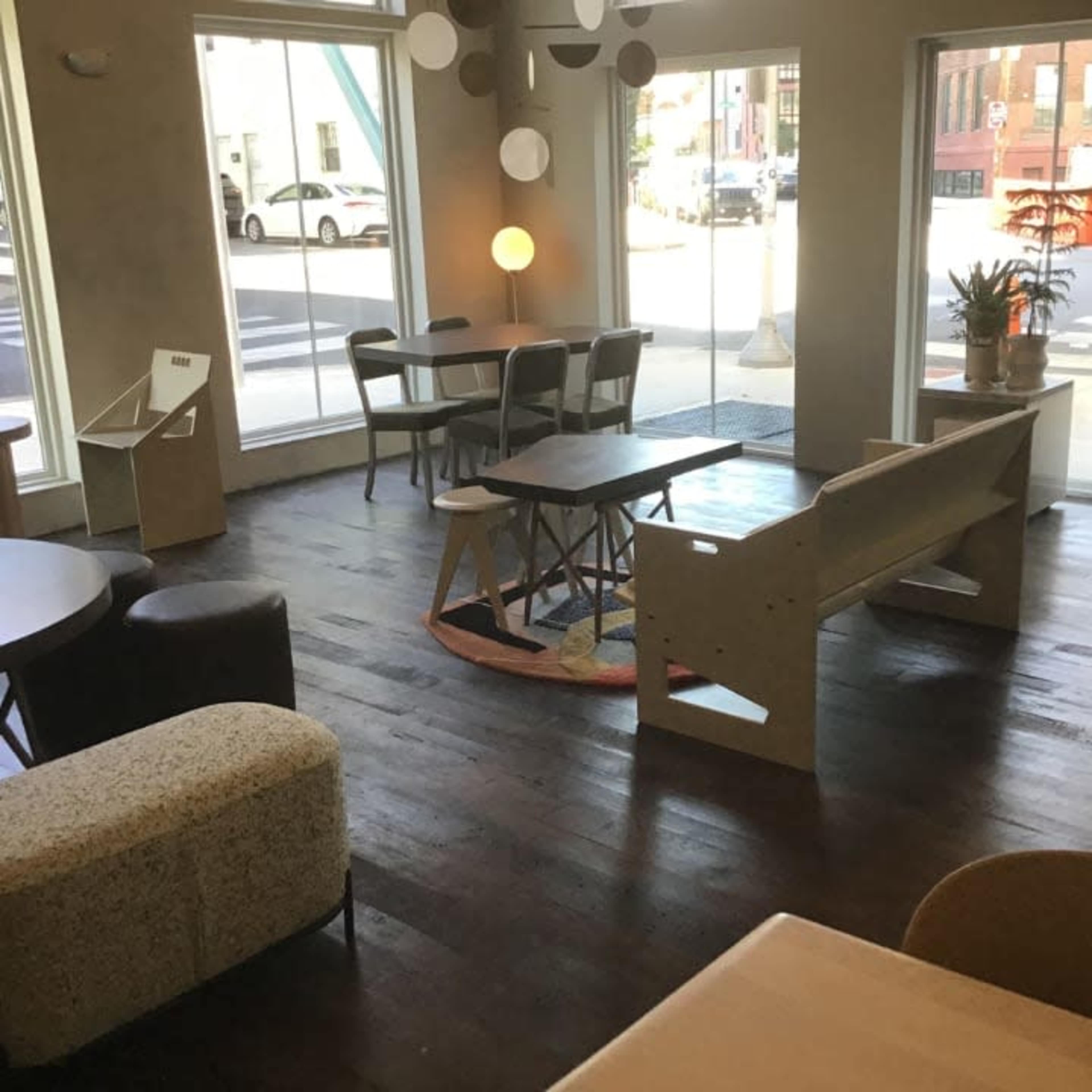 The image shows a modern, minimalist café interior with various seating options and large windows letting in natural light.