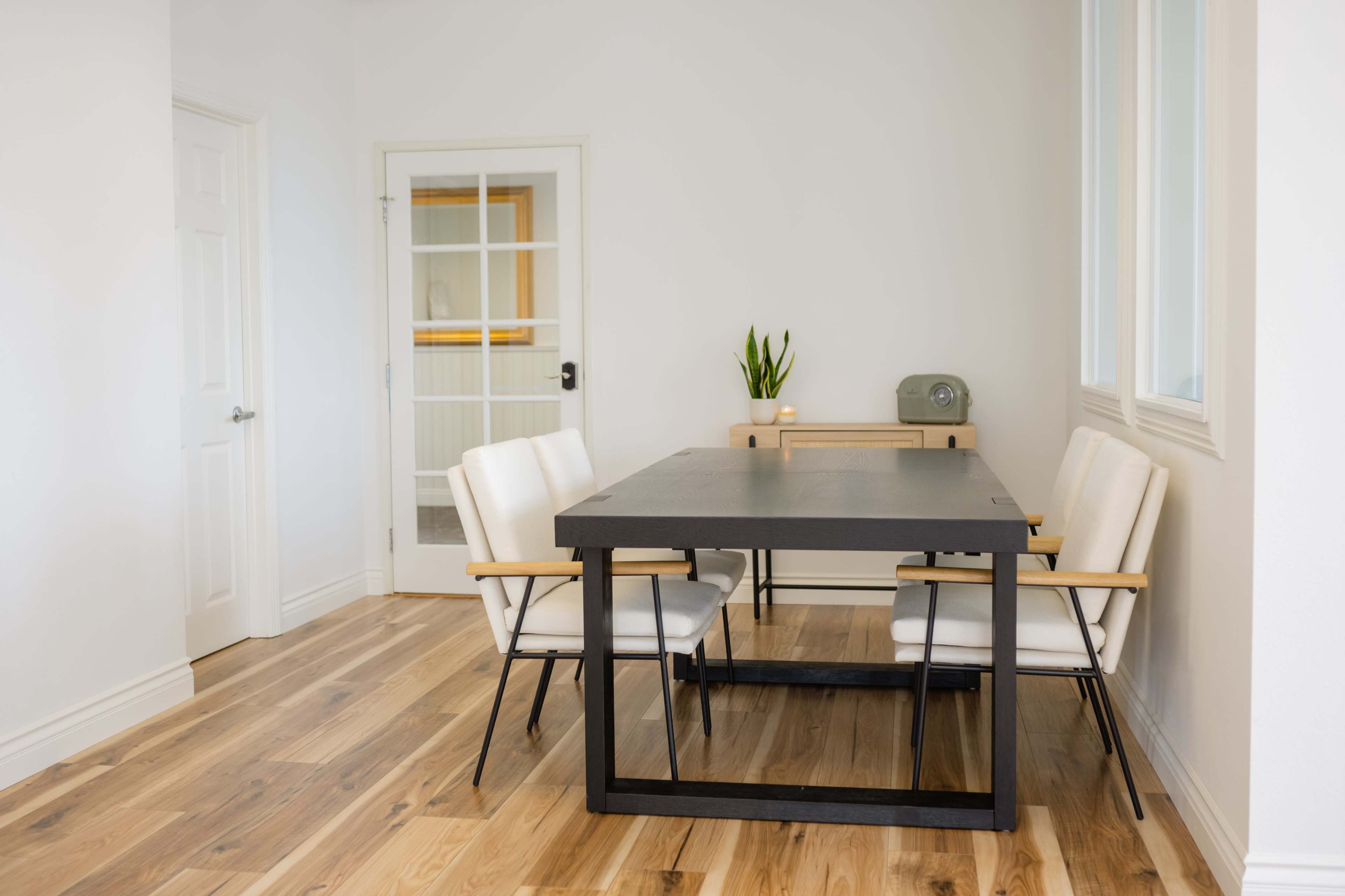 A minimalist dining area features a black rectangular table with four white upholstered chairs and a small green plant on the table.