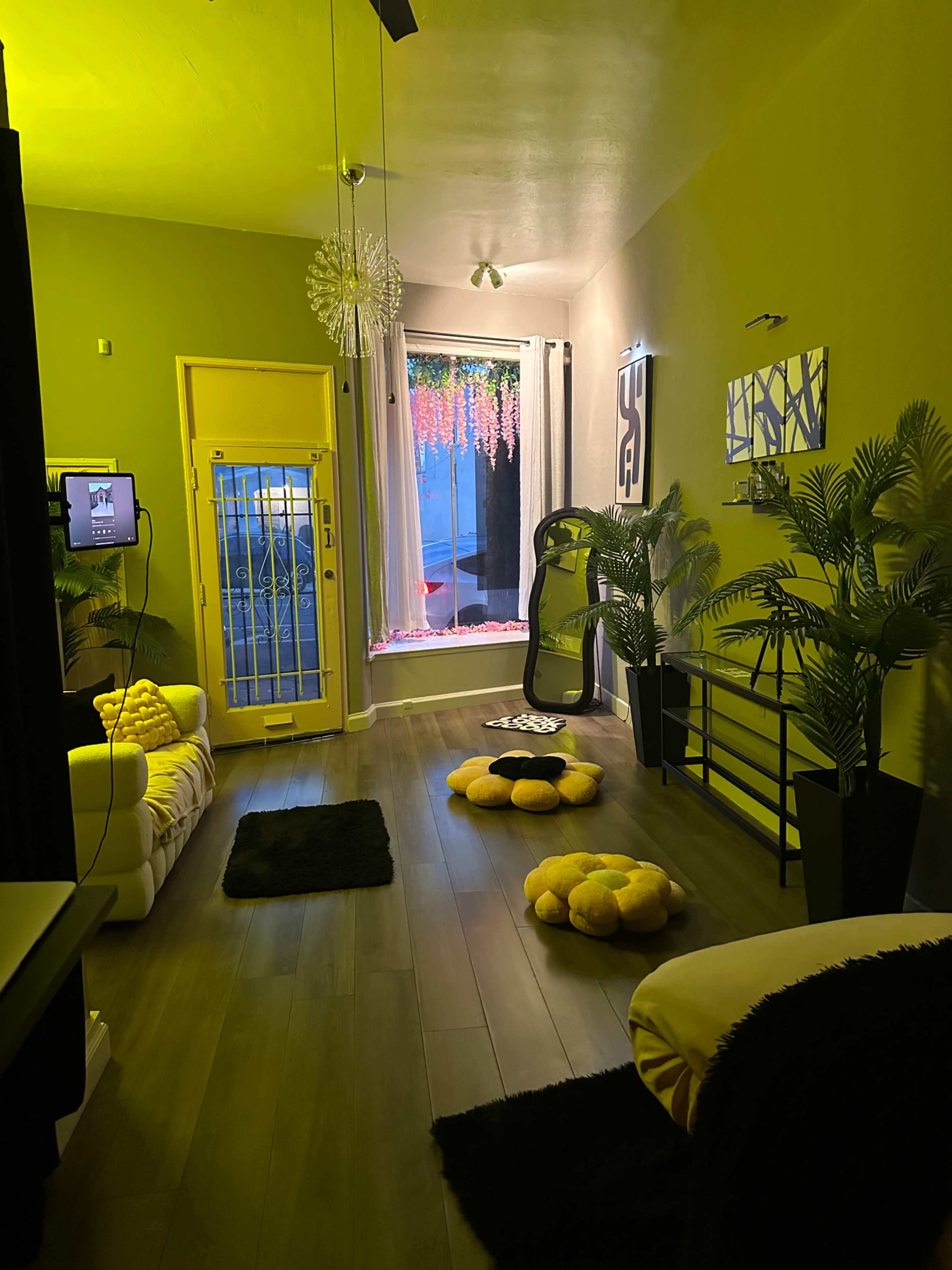 The image features a modern living room with a yellow and gray color scheme, including a large window, plants, and a mix of decor items.