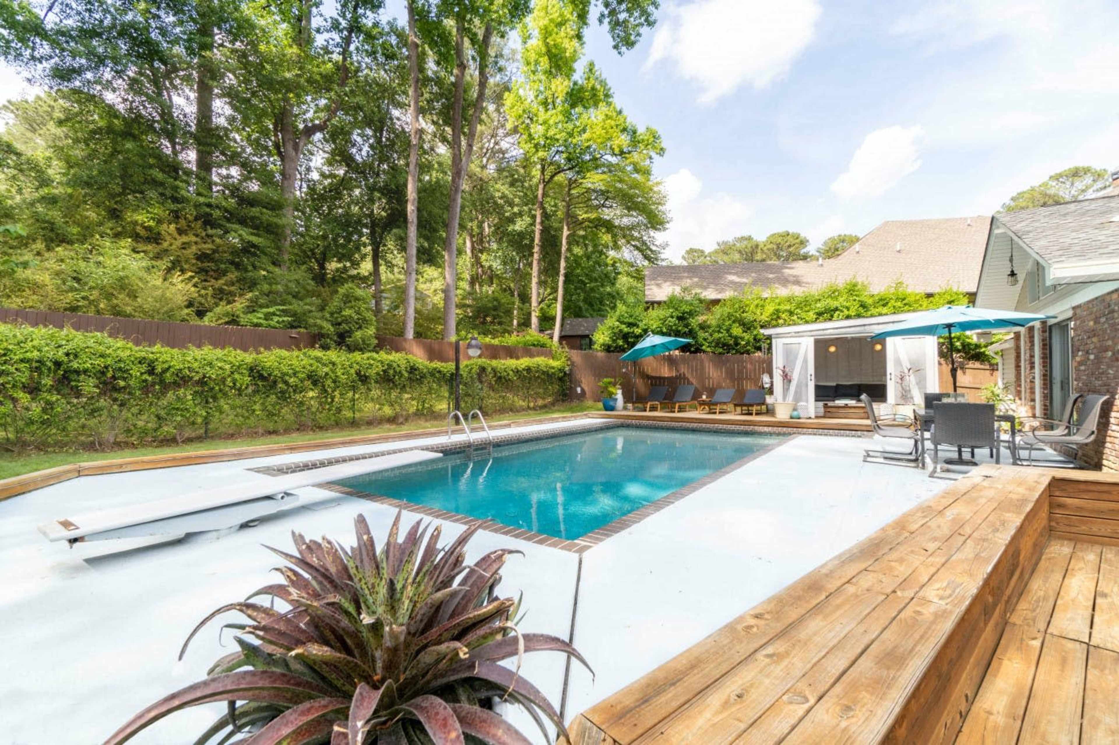 A backyard swimming pool surrounded by a wooden deck, lounge chairs, and green landscaping.