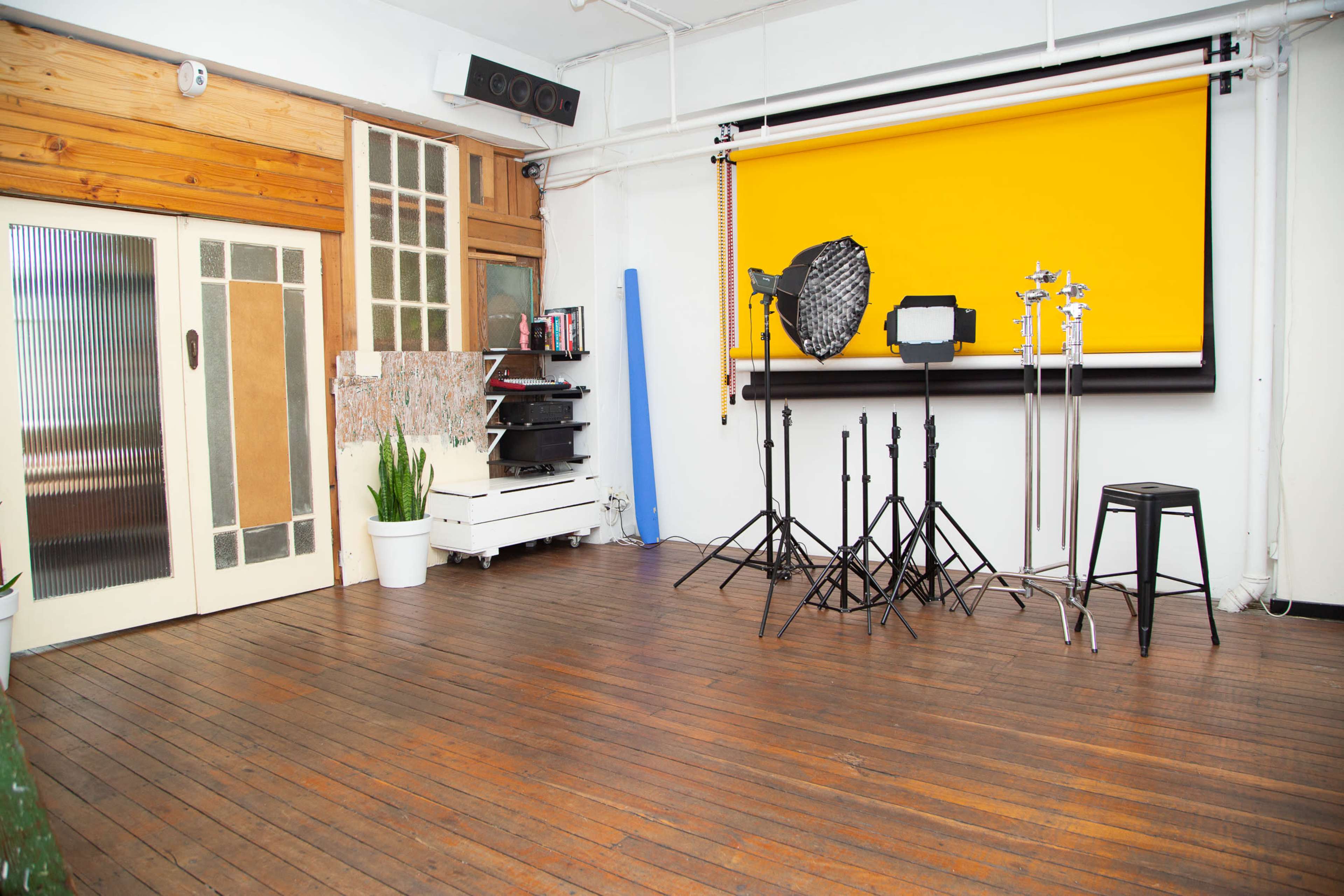 A photography studio with wooden floors, a yellow backdrop, and various lighting equipment set up on stands.