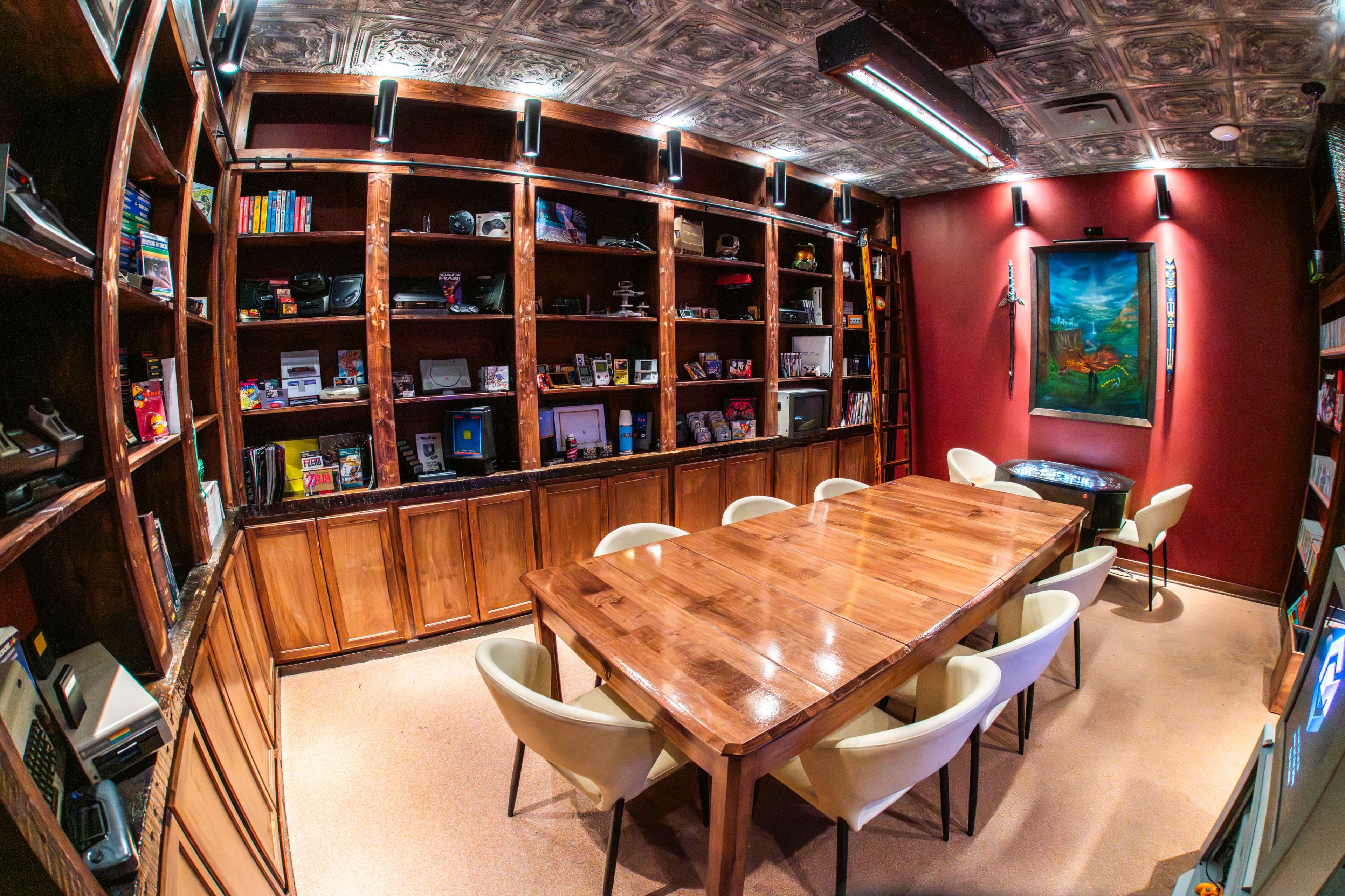 The image shows a modern meeting room with a large wooden table surrounded by white chairs, flanked by shelves filled with various items and decorations, against a backdrop of dark red walls.