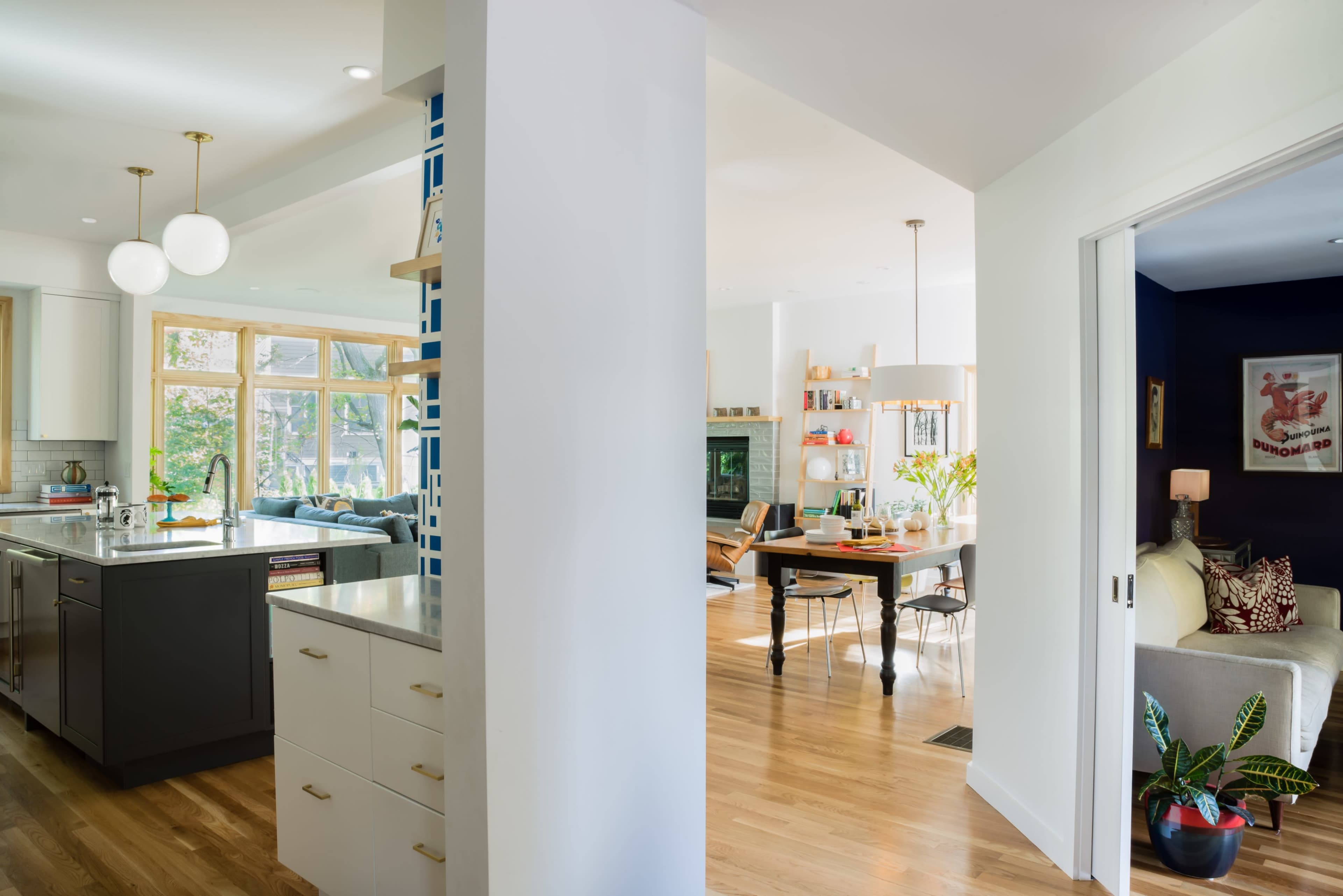 A modern open-plan kitchen and living area features a large window, light wood flooring, and contemporary furnishings.
