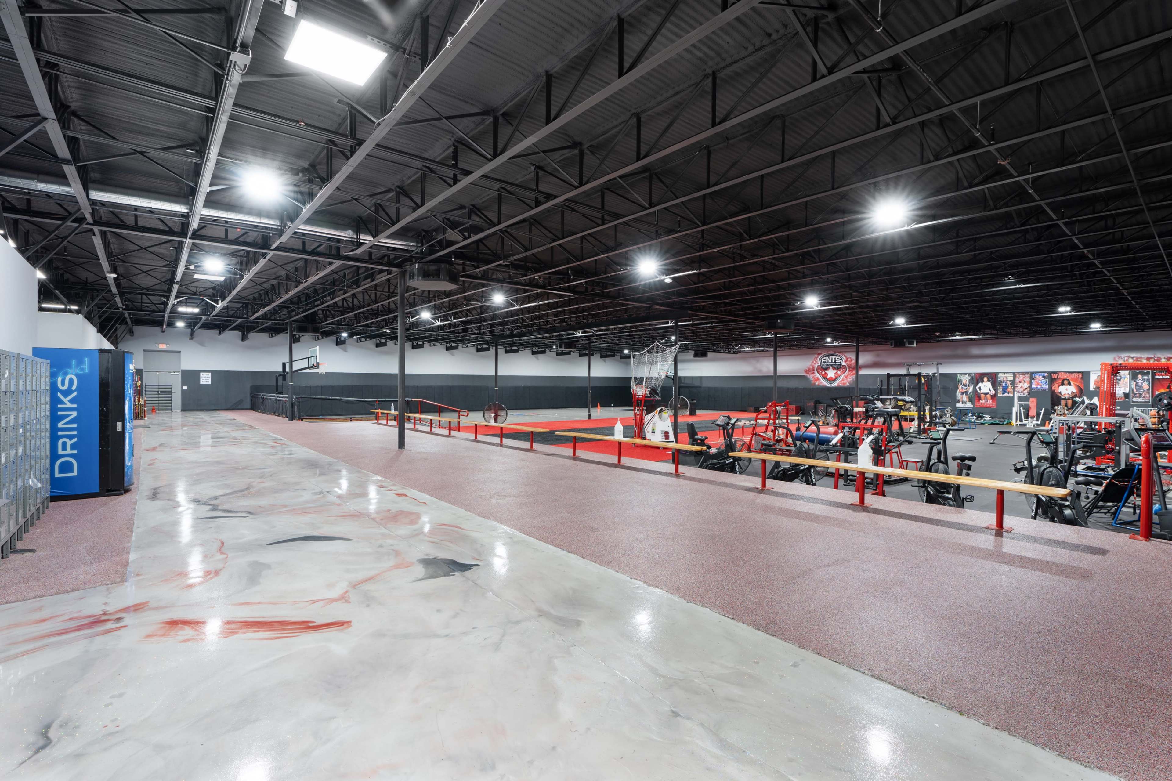 A spacious gym interior featuring various exercise equipment, a basketball hoop, and a long rubberized flooring area.