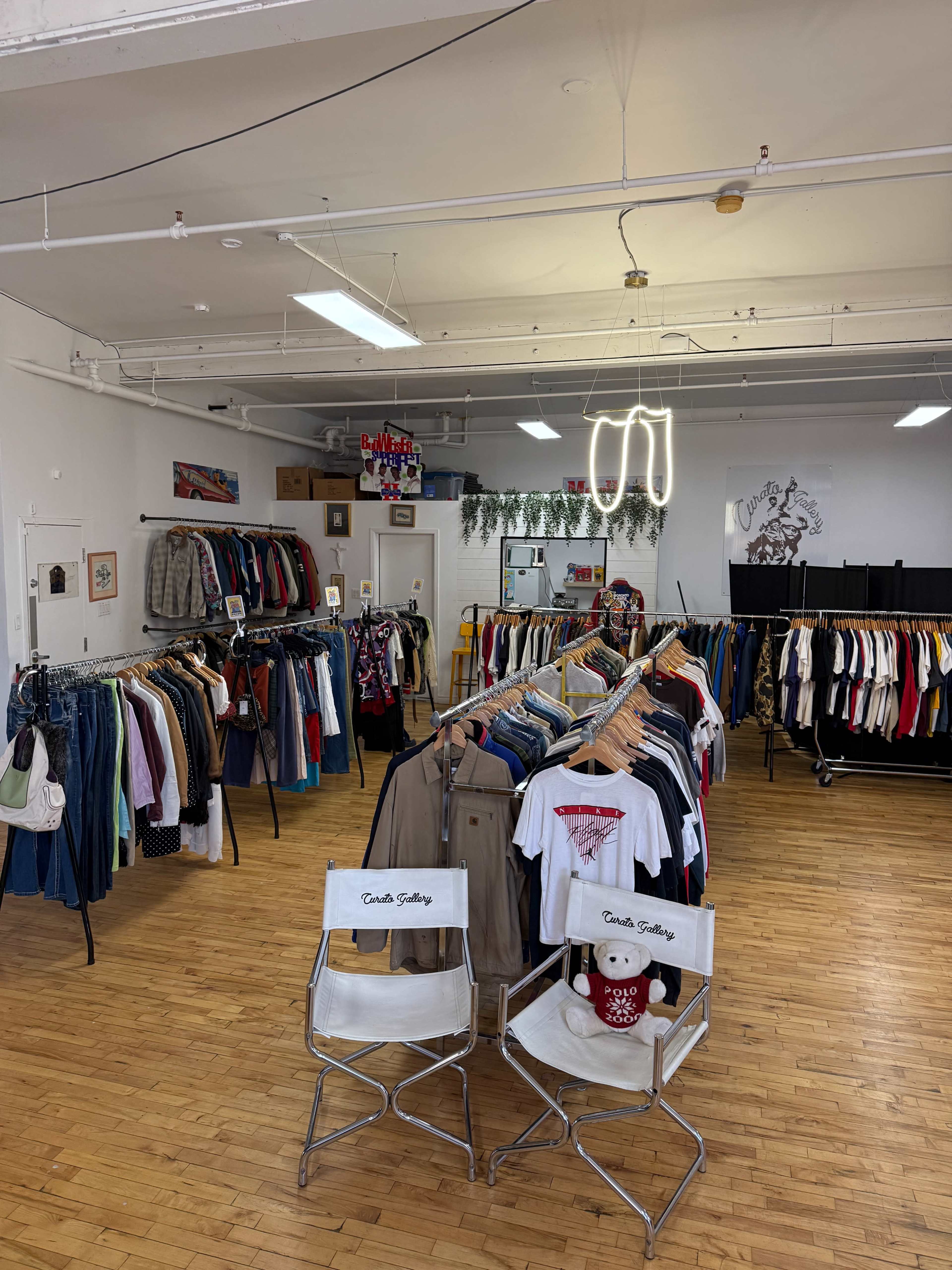 The image shows a vintage clothing store with racks of assorted clothing and two director's chairs in the foreground.
