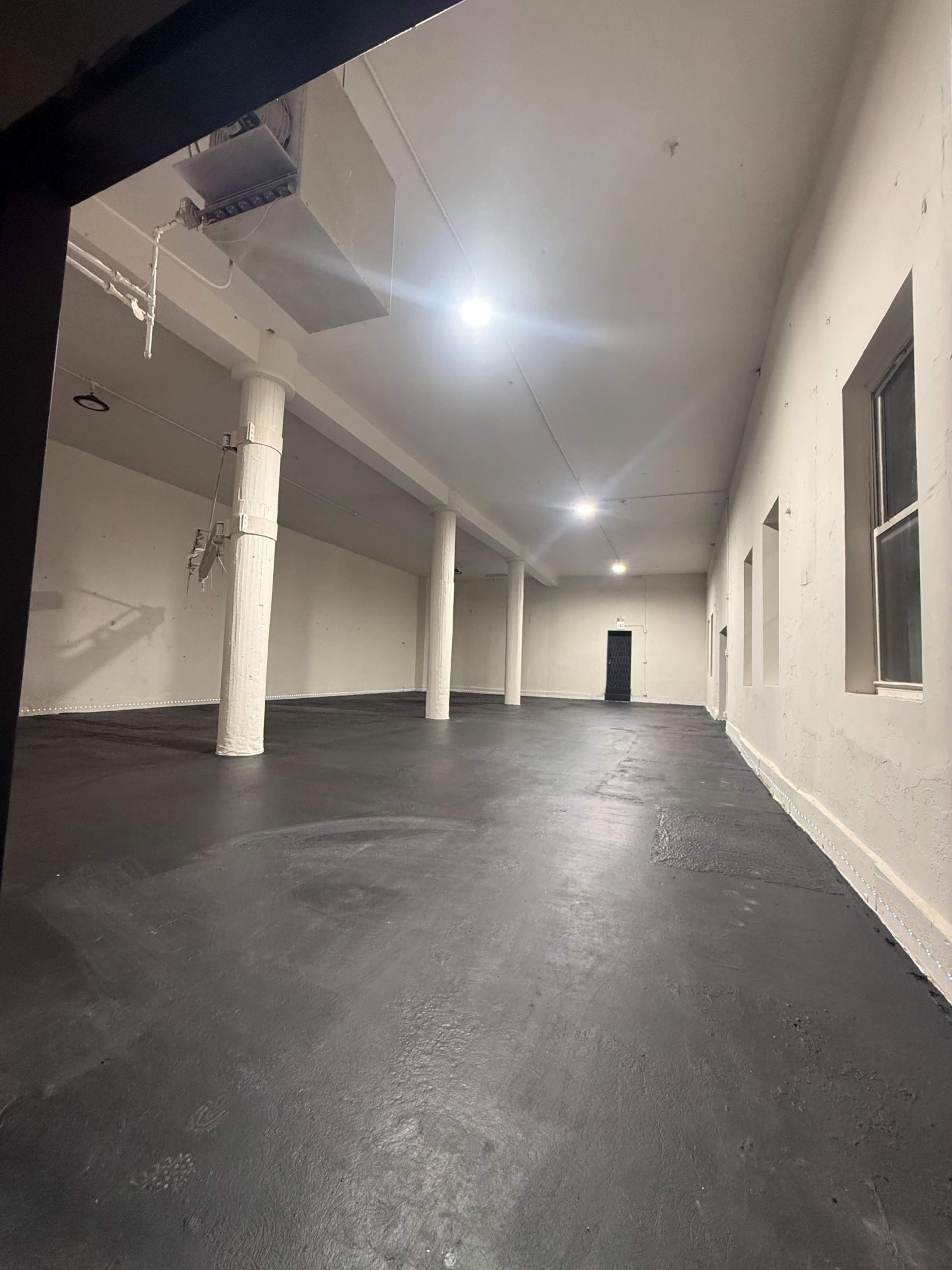 The image shows an empty, spacious interior room with a polished black floor, white walls, and several columns.