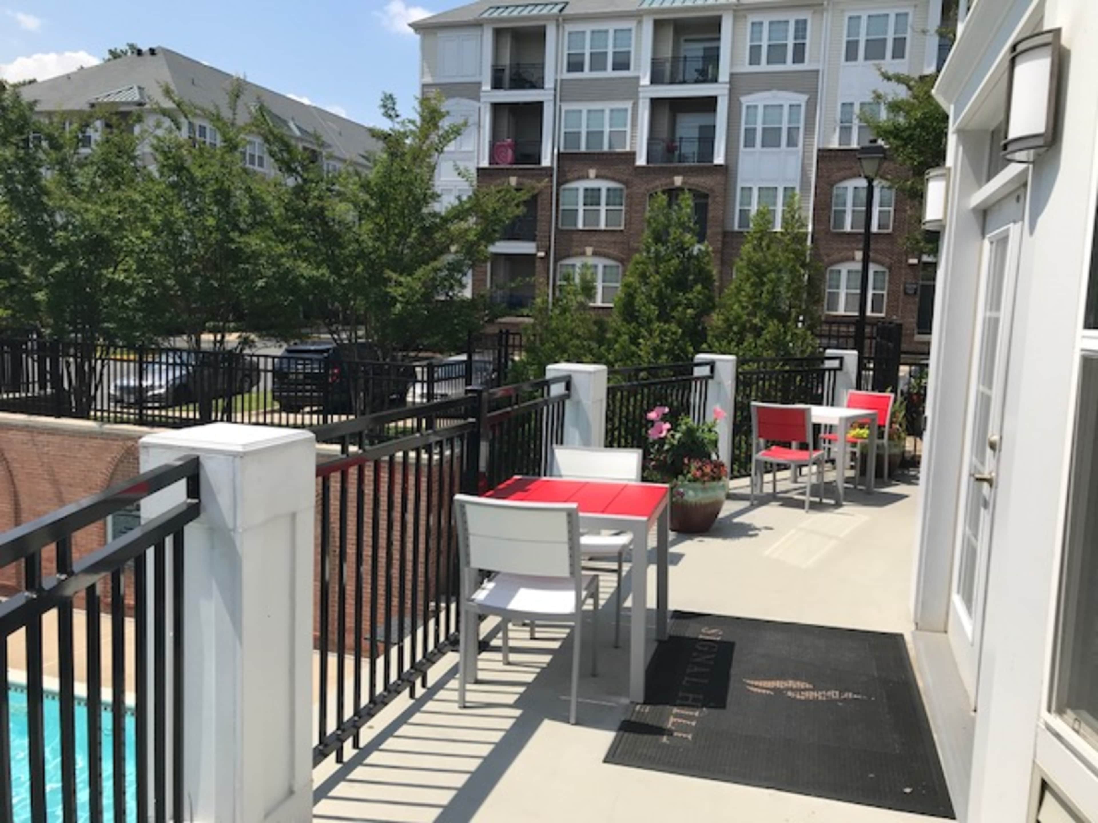 The image shows a poolside area with tables and chairs, alongside a residential apartment building.