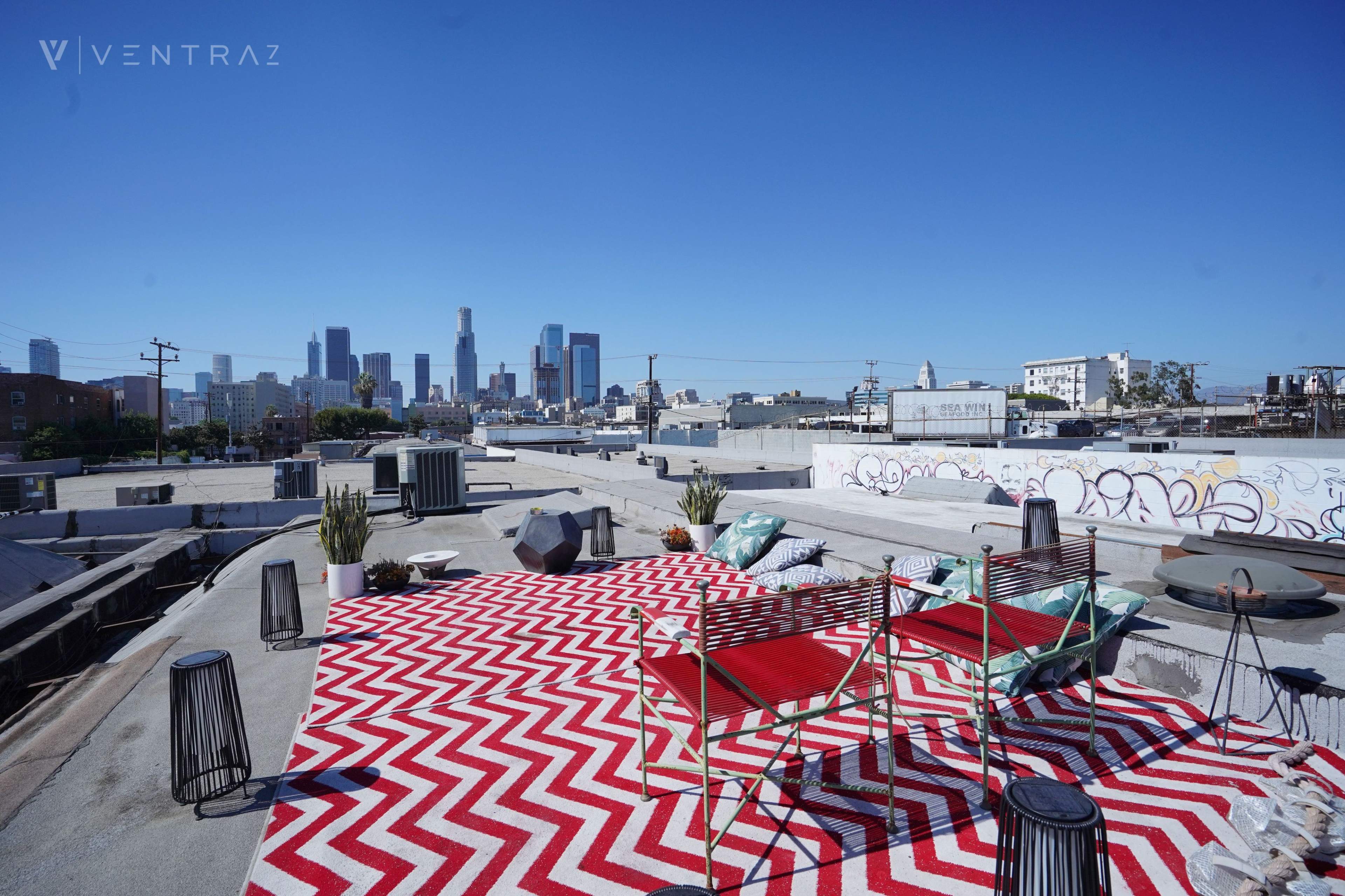 A rooftop terrace with a red and white zigzag rug, two chairs, plants, and a view of the Los Angeles skyline.