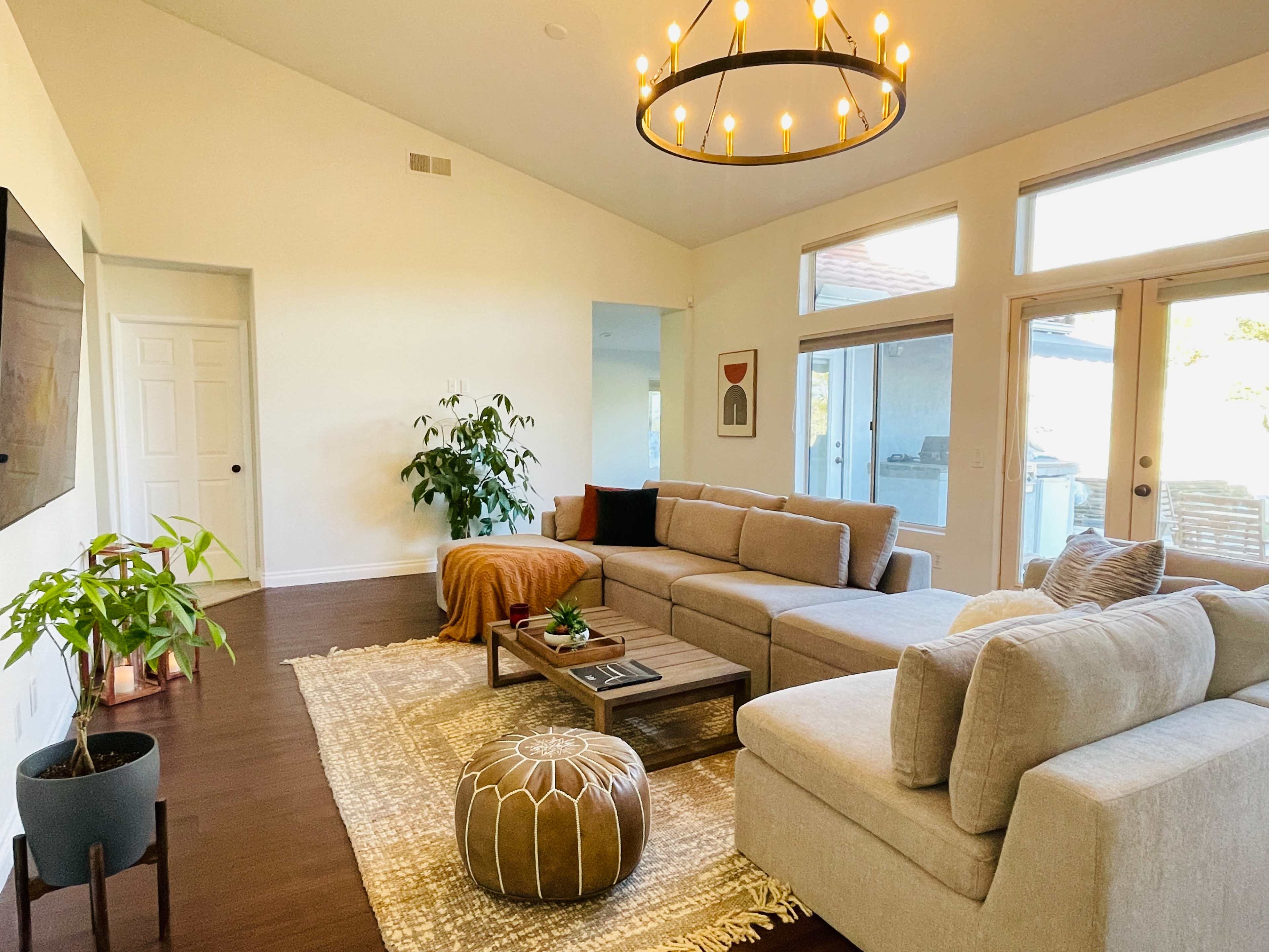 A modern living room featuring a sectional sofa, a coffee table on a patterned rug, and large windows allowing natural light to enter the space.