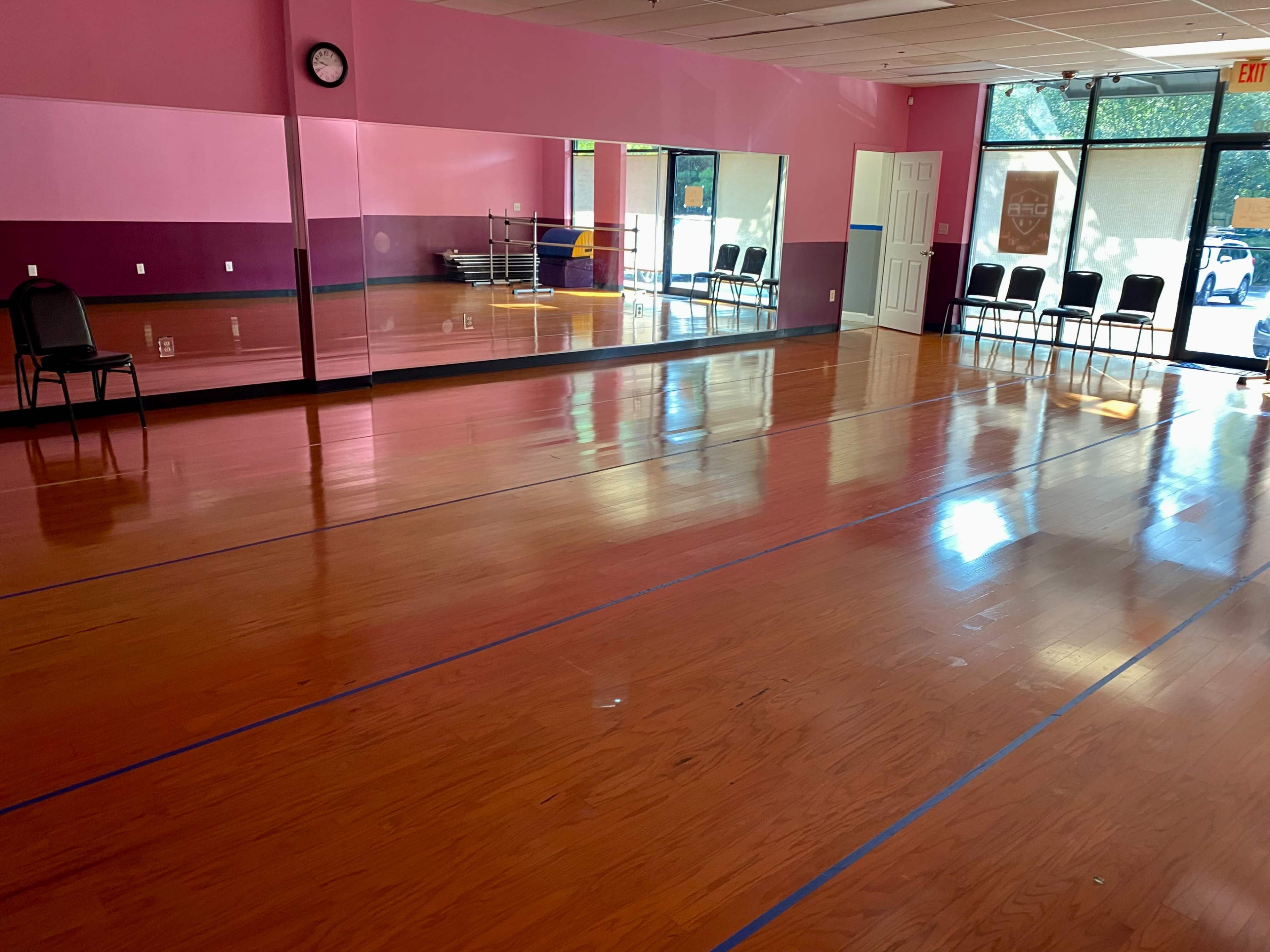 A dance studio features a wooden floor, mirrored wall, and rows of chairs along one side.