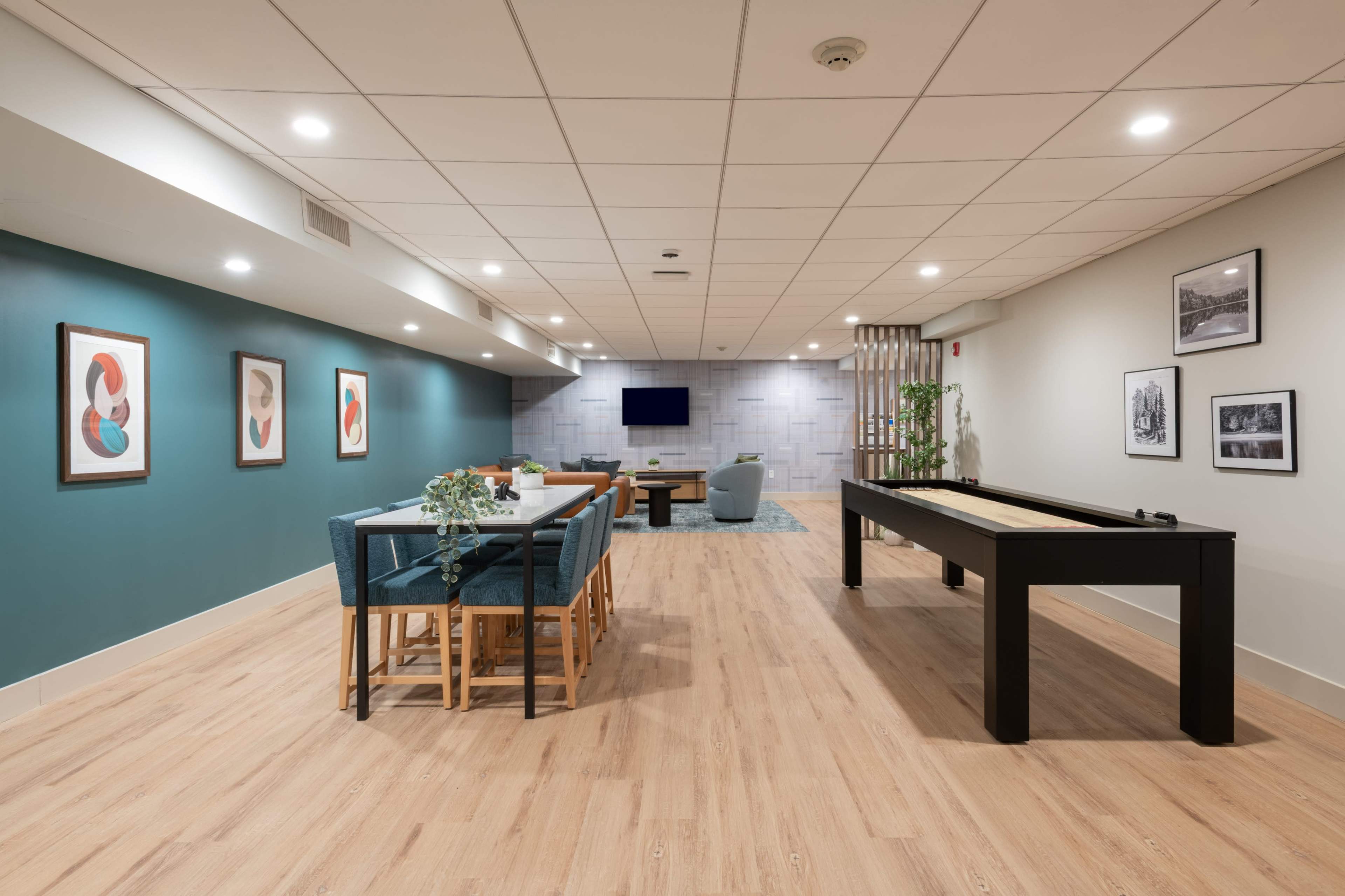 The image shows a spacious, modern game room featuring a pool table, a dining area with seating, and a large flat-screen TV on the wall.