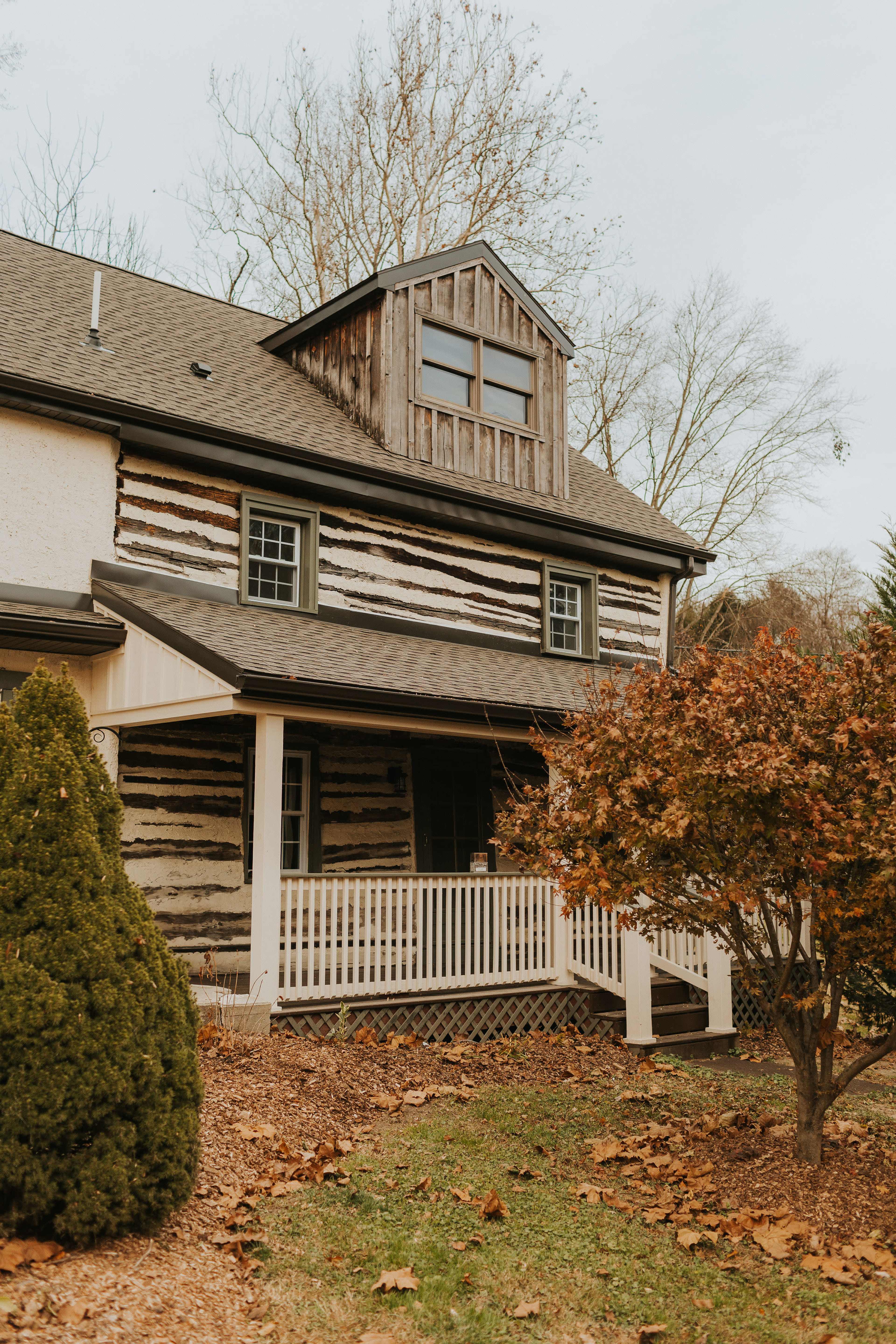 A log cabin-style house with a gabled roof, a front porch, and trees in the vicinity.