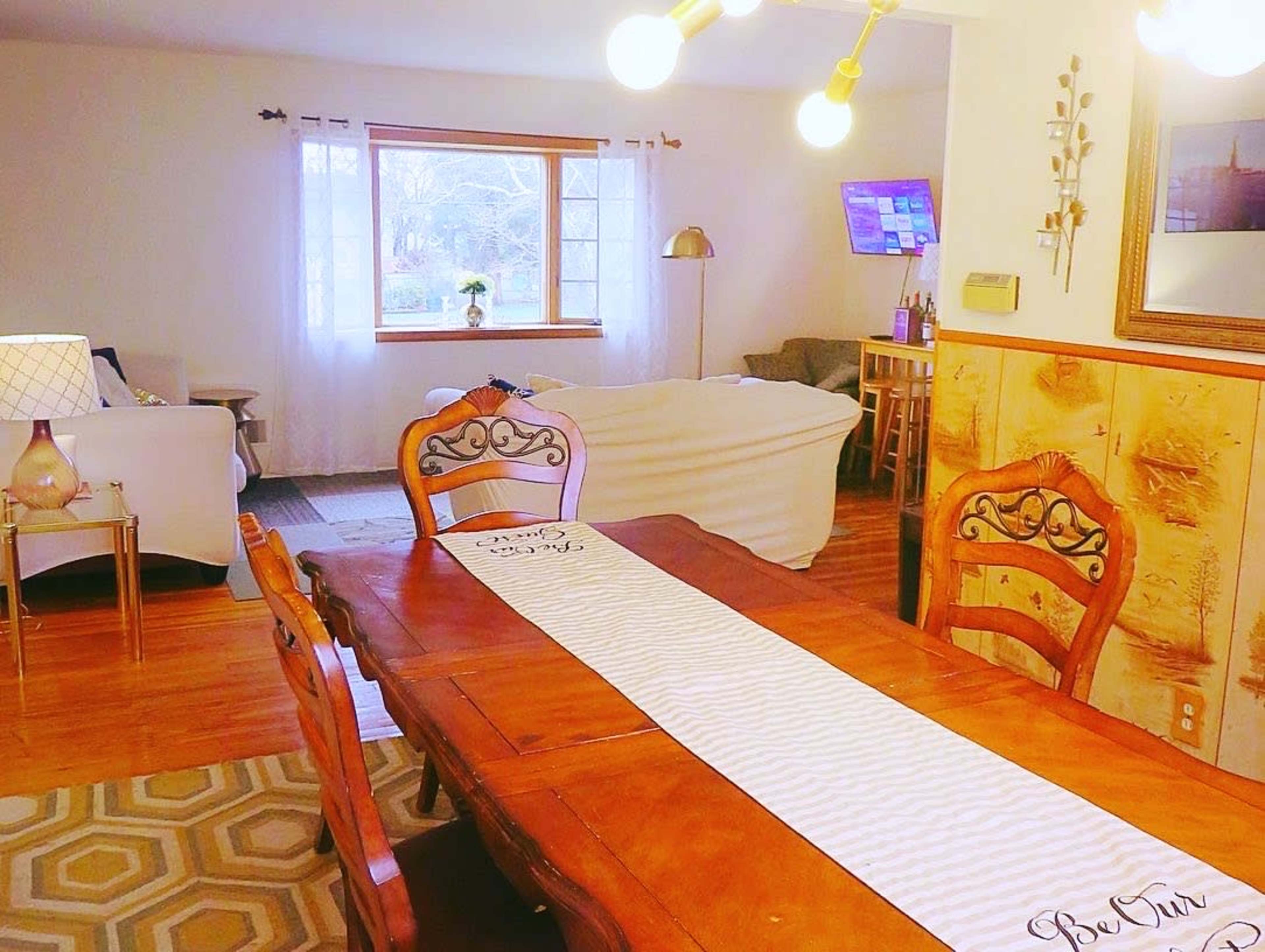 A wooden dining table with decorative runners is positioned in a cozy room that includes a seating area and a window.