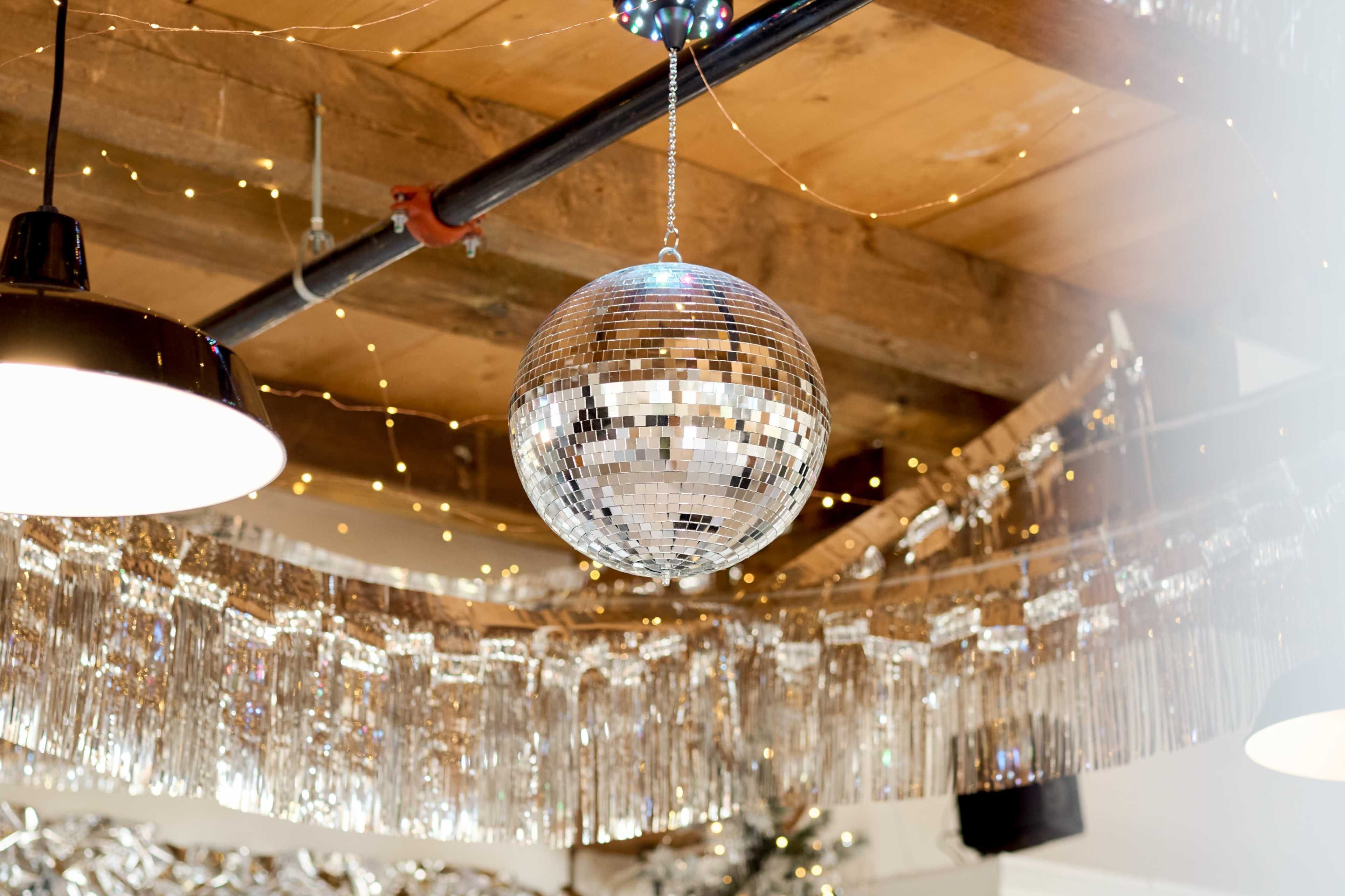 A mirrored disco ball hangs from the ceiling, surrounded by string lights and metallic decorations.