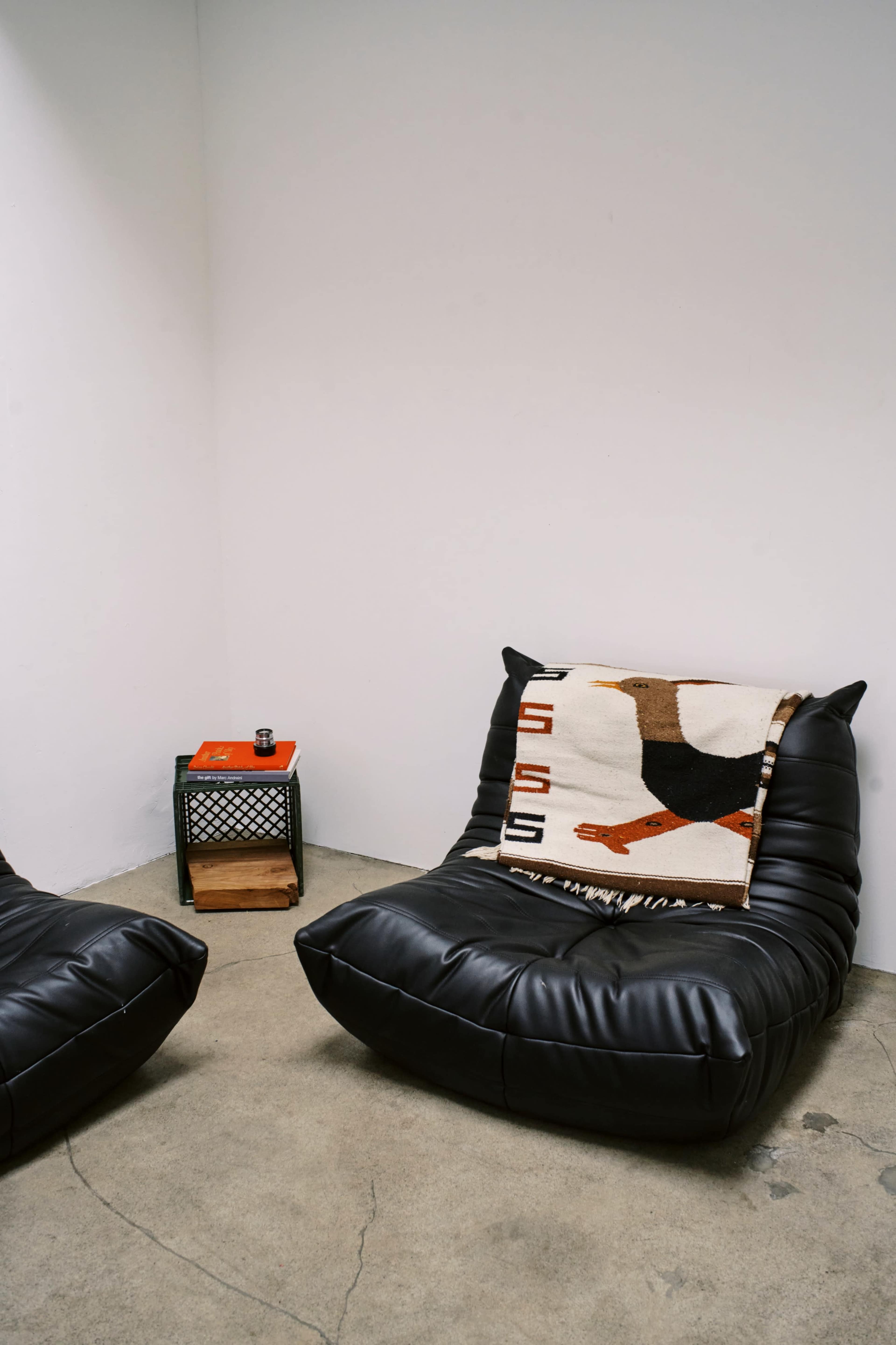 The image shows two black cushioned chairs with a blanket featuring a bird design draped over one, next to a small side table.