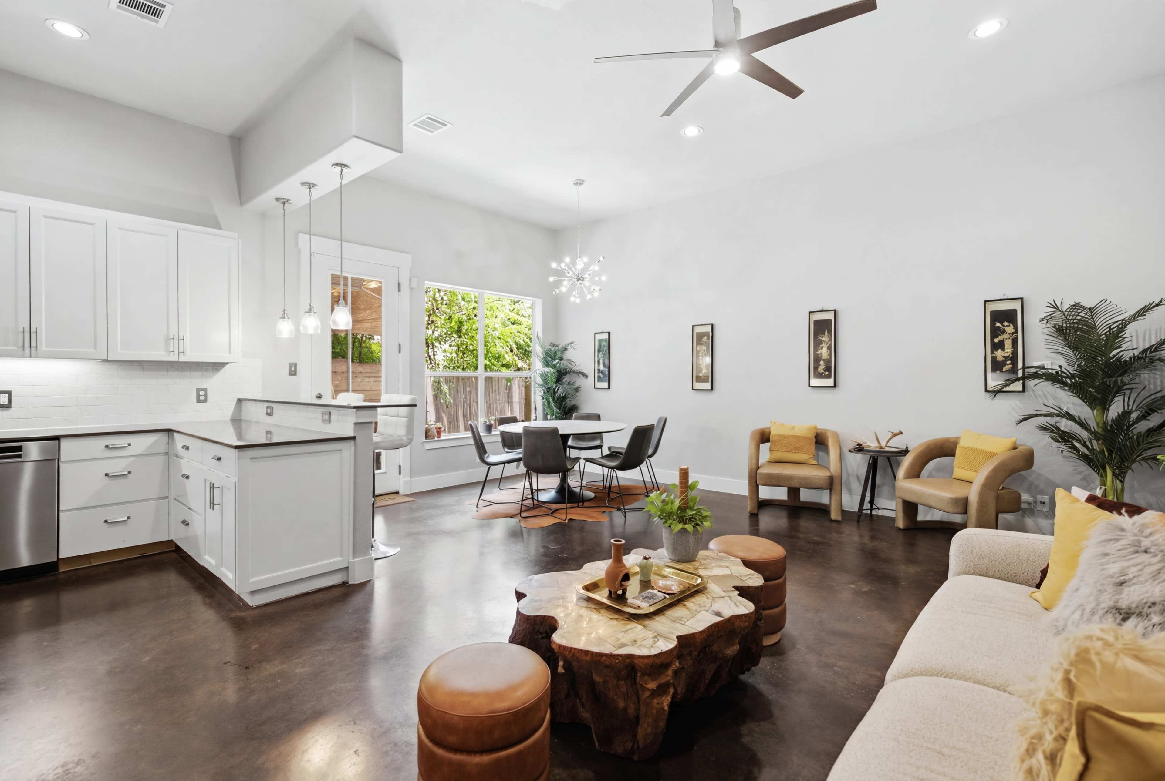 The image shows a modern, open-concept living area featuring a kitchen island, dining space, and a comfortable seating area, all with contemporary furnishings and decor.