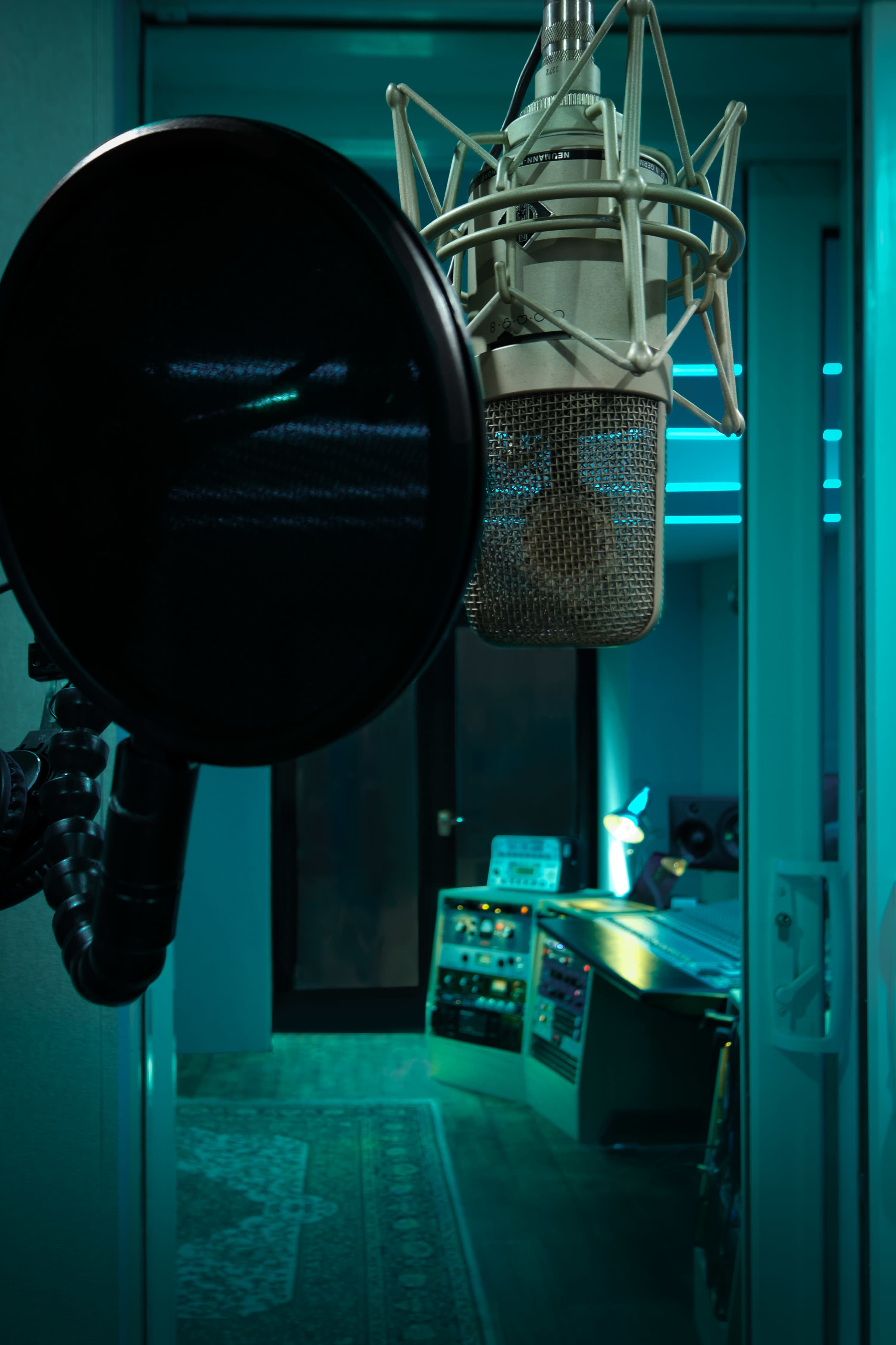 The image shows a microphone with a pop filter in the foreground and a dimly lit recording studio in the background.