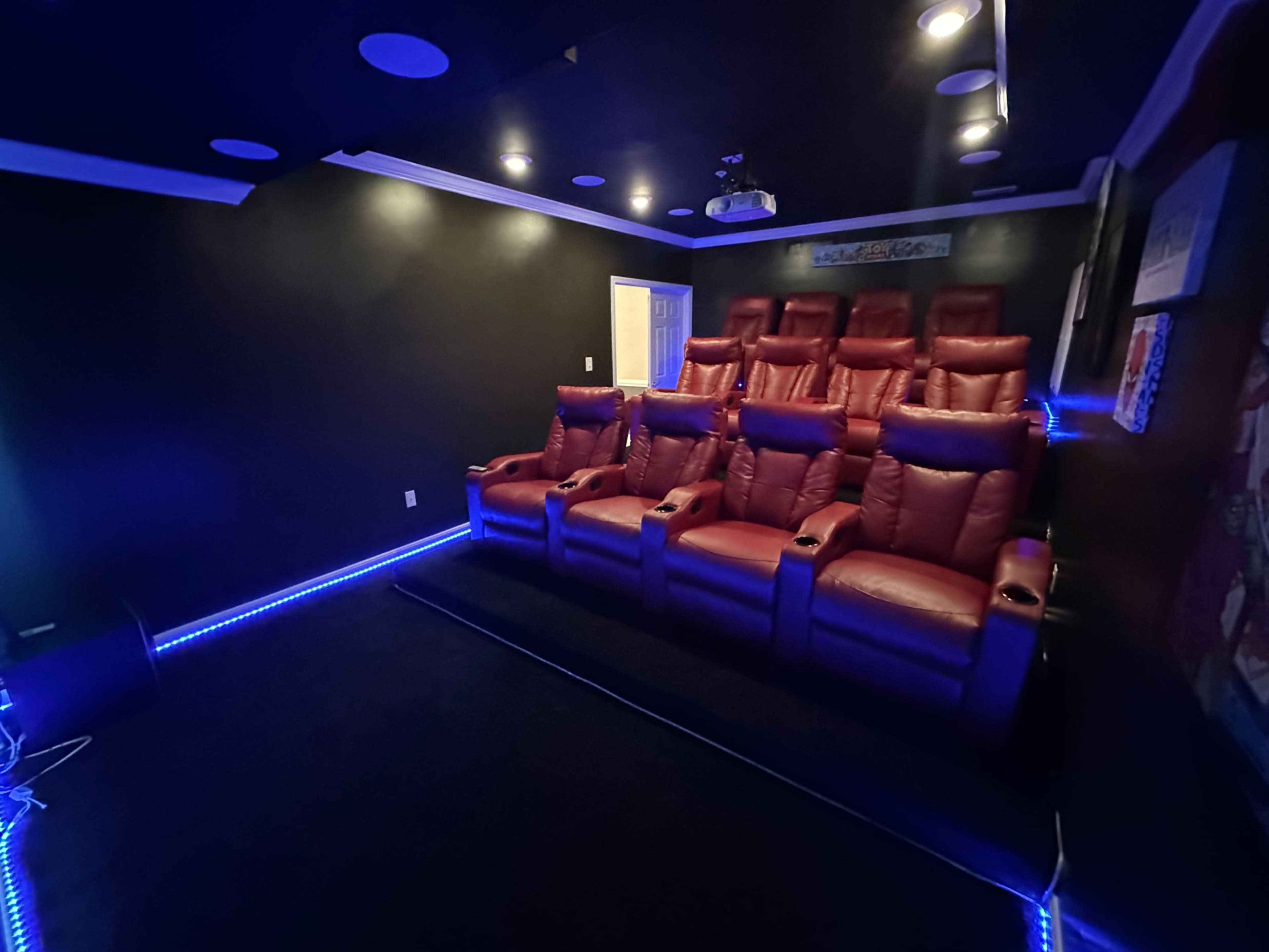 An intimate home theater with seven red reclining seats arranged in a dark room, illuminated by blue LED lighting along the floor.