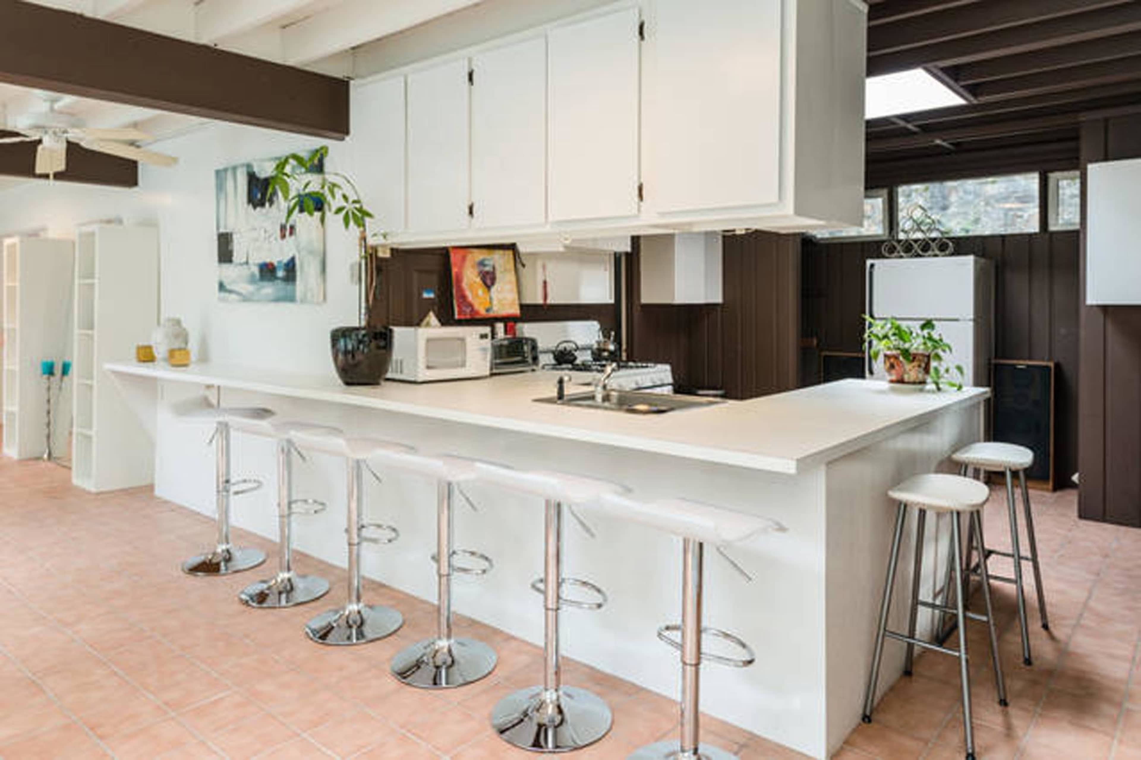 The image shows a modern kitchen with a large white island, bar stools, and a wall of cabinets.