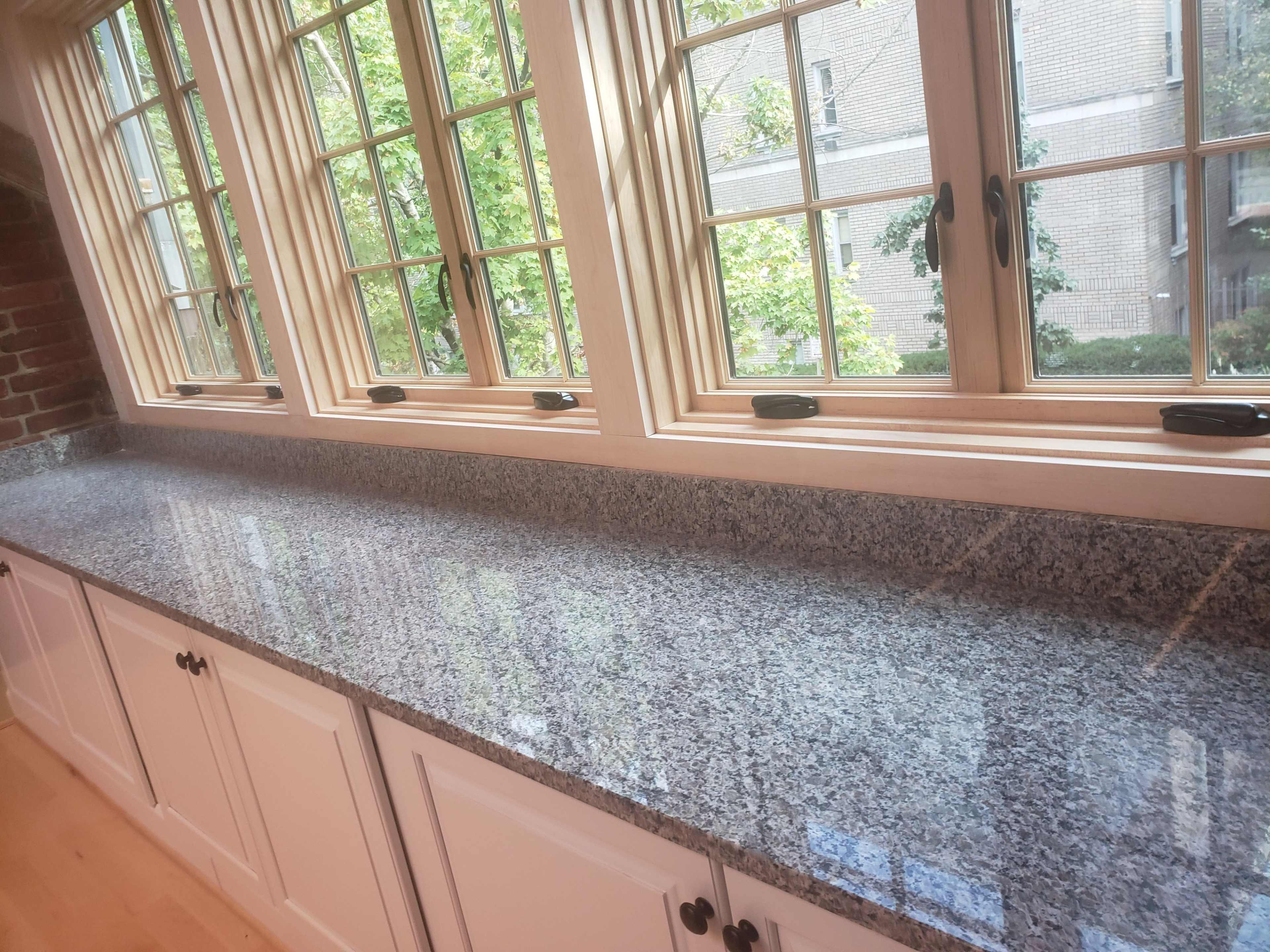A kitchen countertop made of speckled gray granite with a row of windows overlooking greenery.