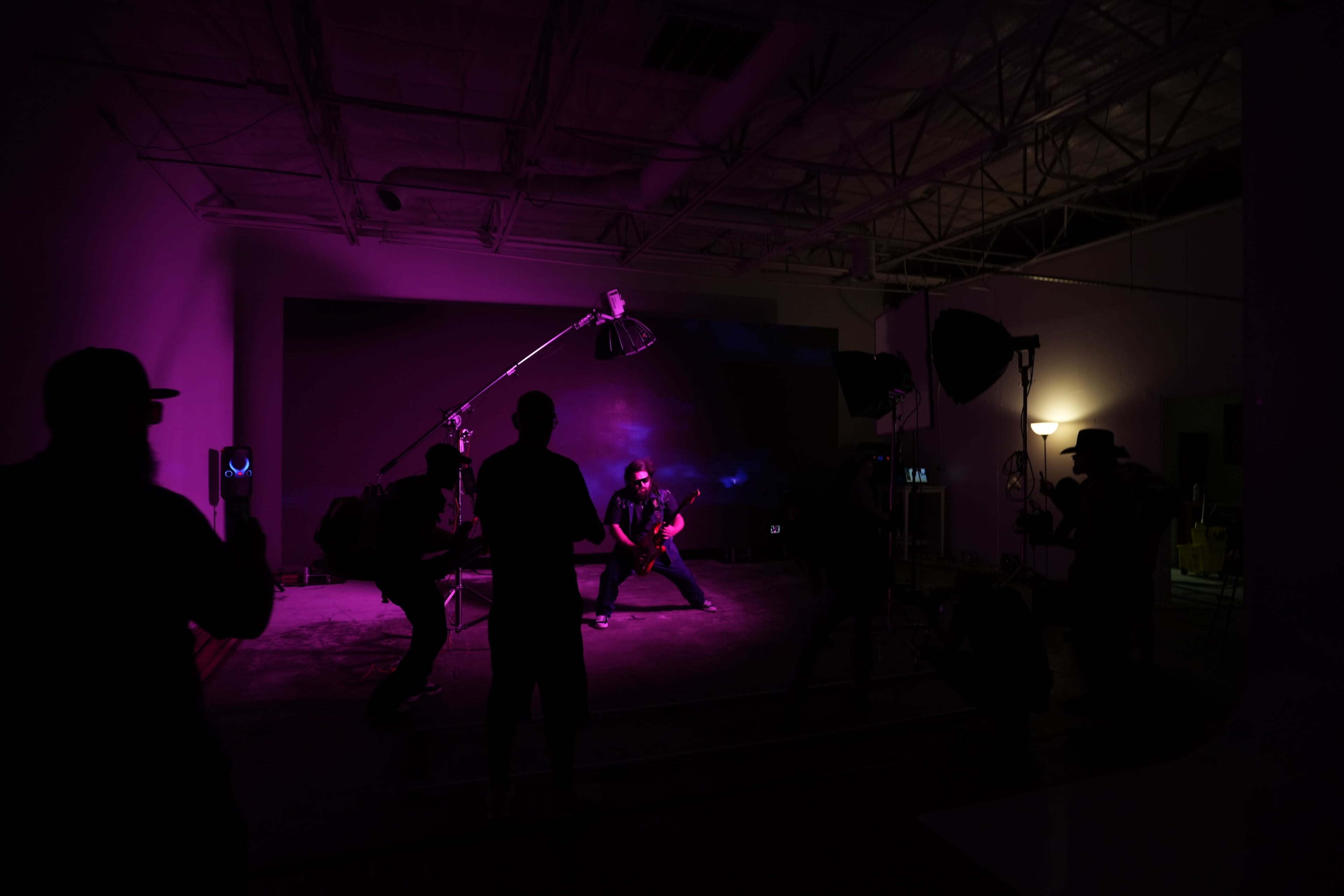A group of photographers is capturing images of a performer in a dimly lit studio with purple lighting.