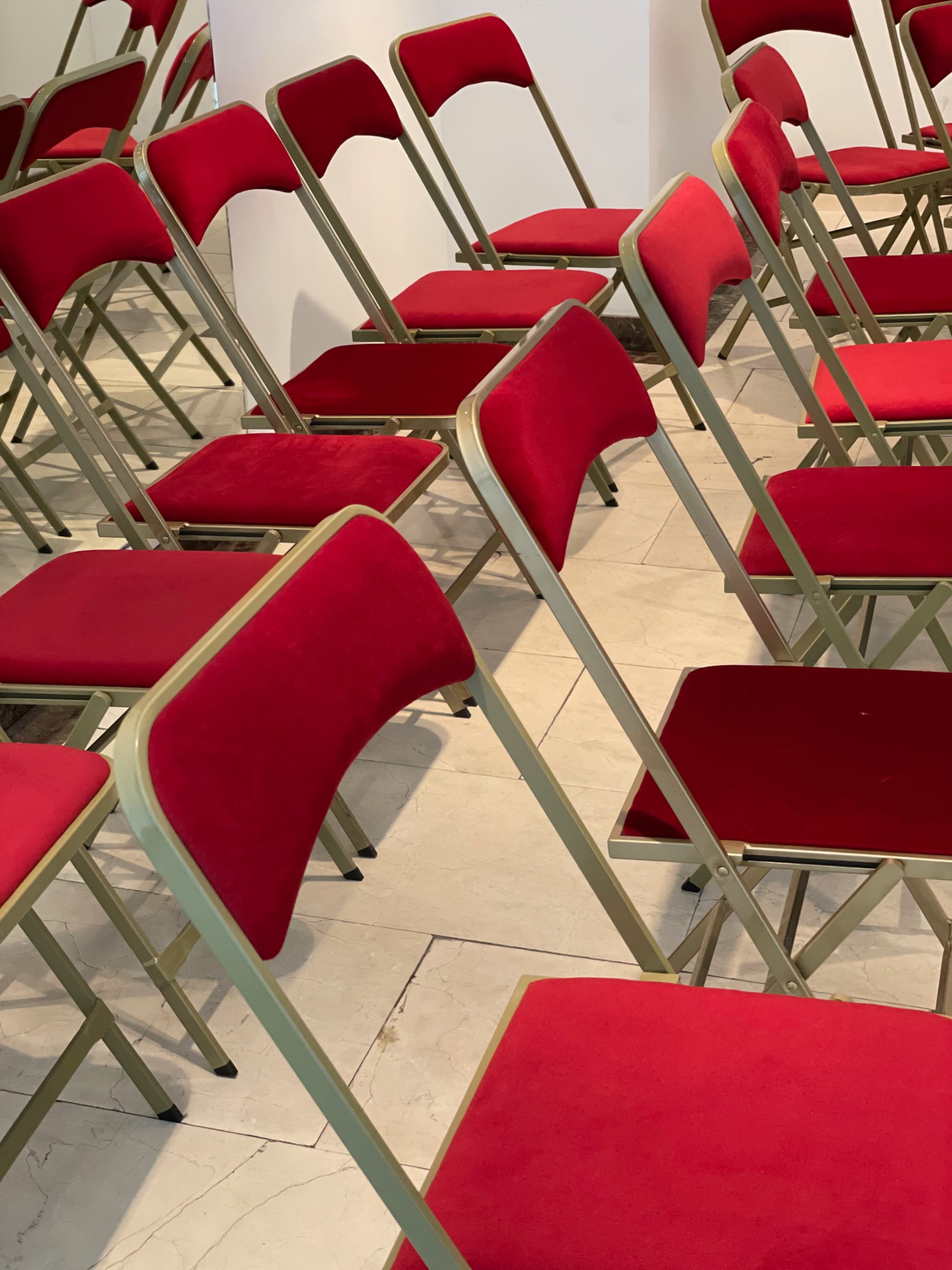 A row of red fabric folding chairs is arranged on a tiled floor.