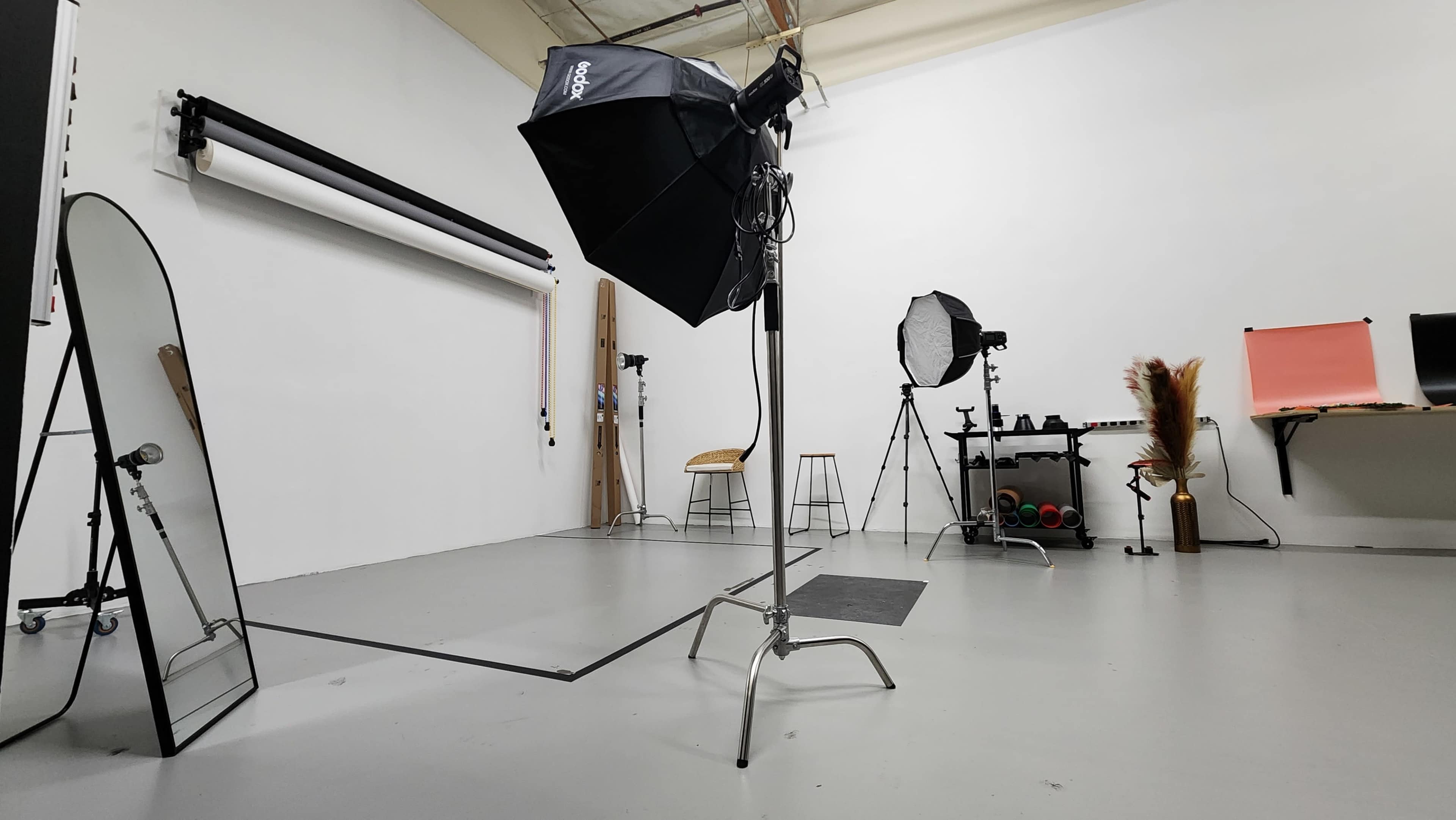 A photography studio with various lighting equipment, a large mirror, and backdrops set up against a white wall.