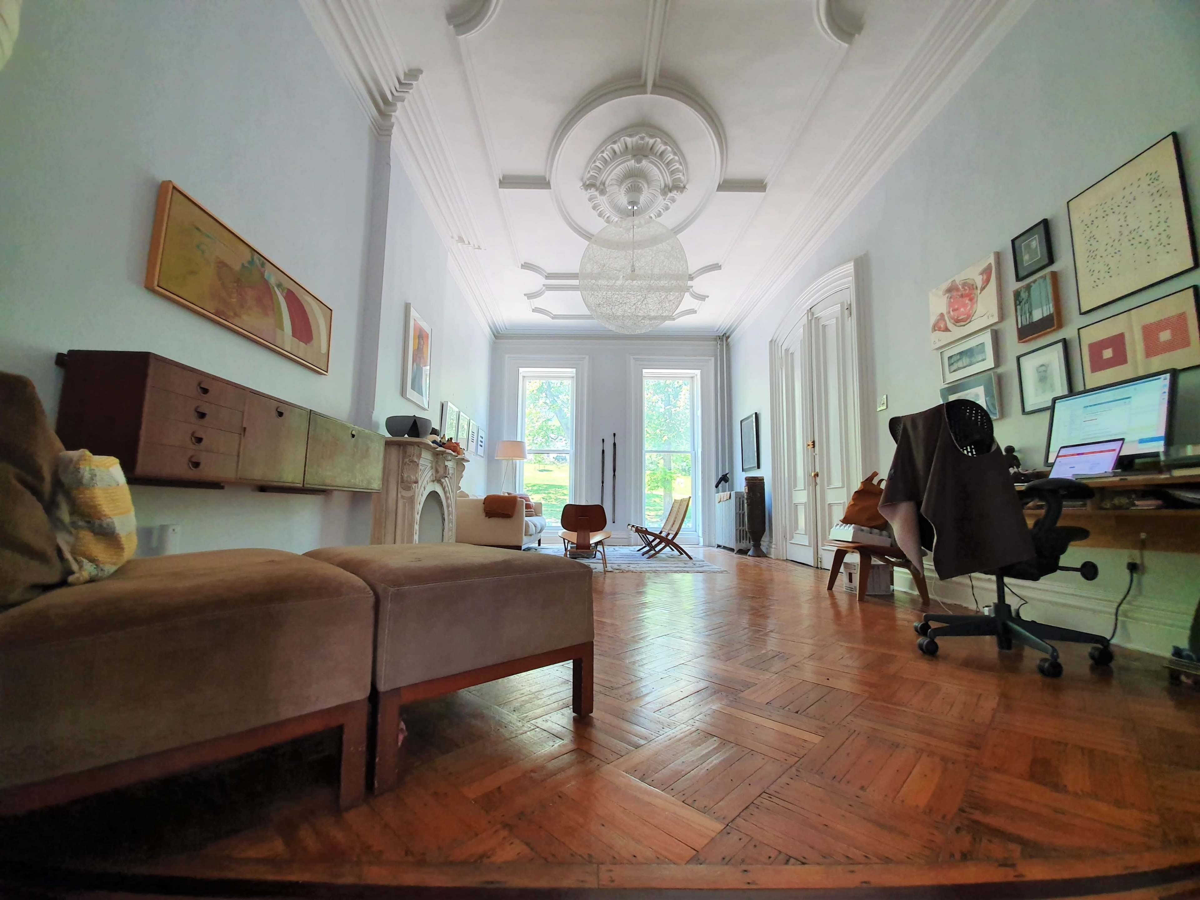 A spacious interior features a mix of vintage and modern furniture, parquet flooring, and large windows that let in natural light.