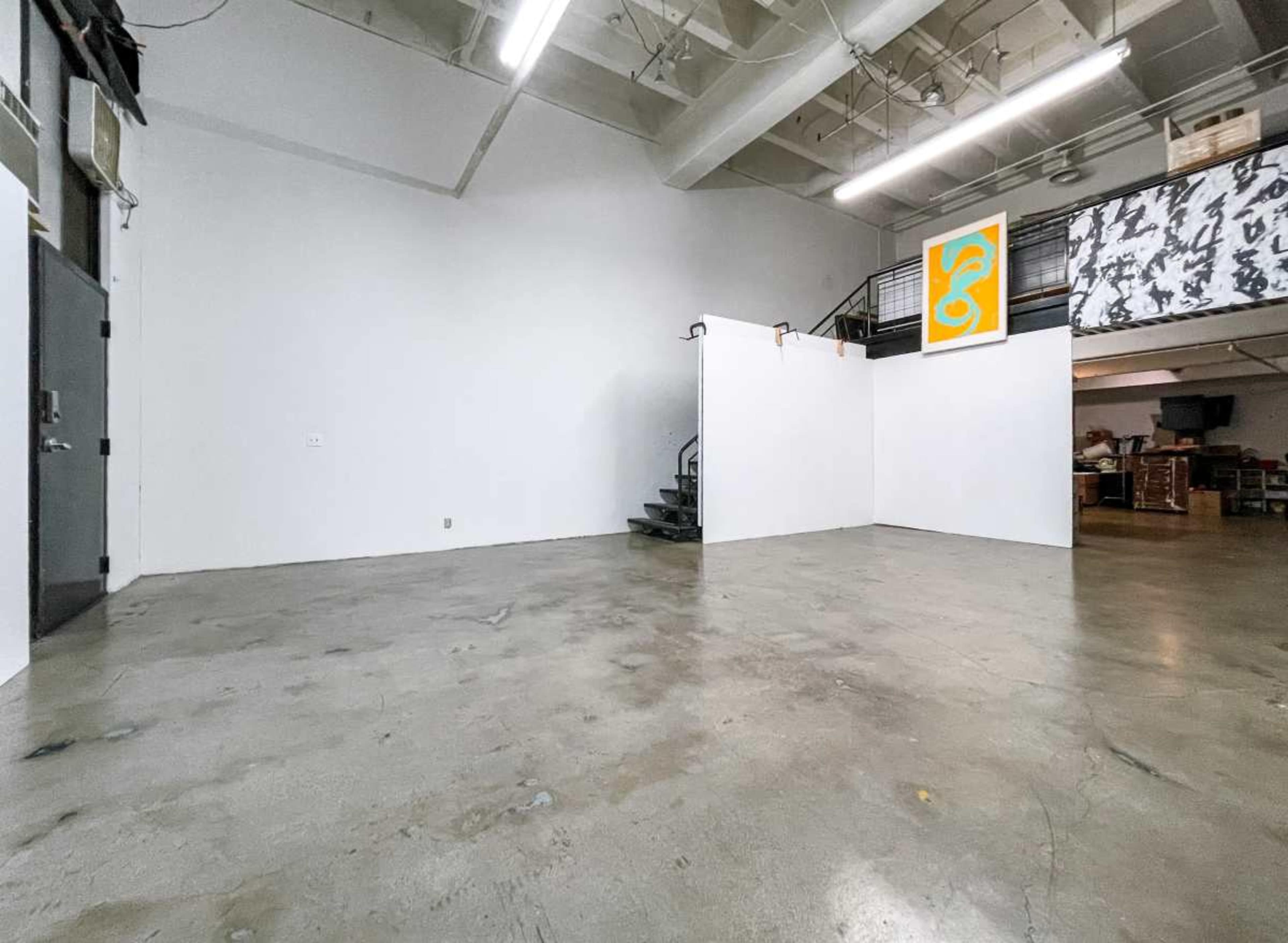 The image shows an empty industrial-style room with a polished concrete floor and a staircase leading to an upper level.