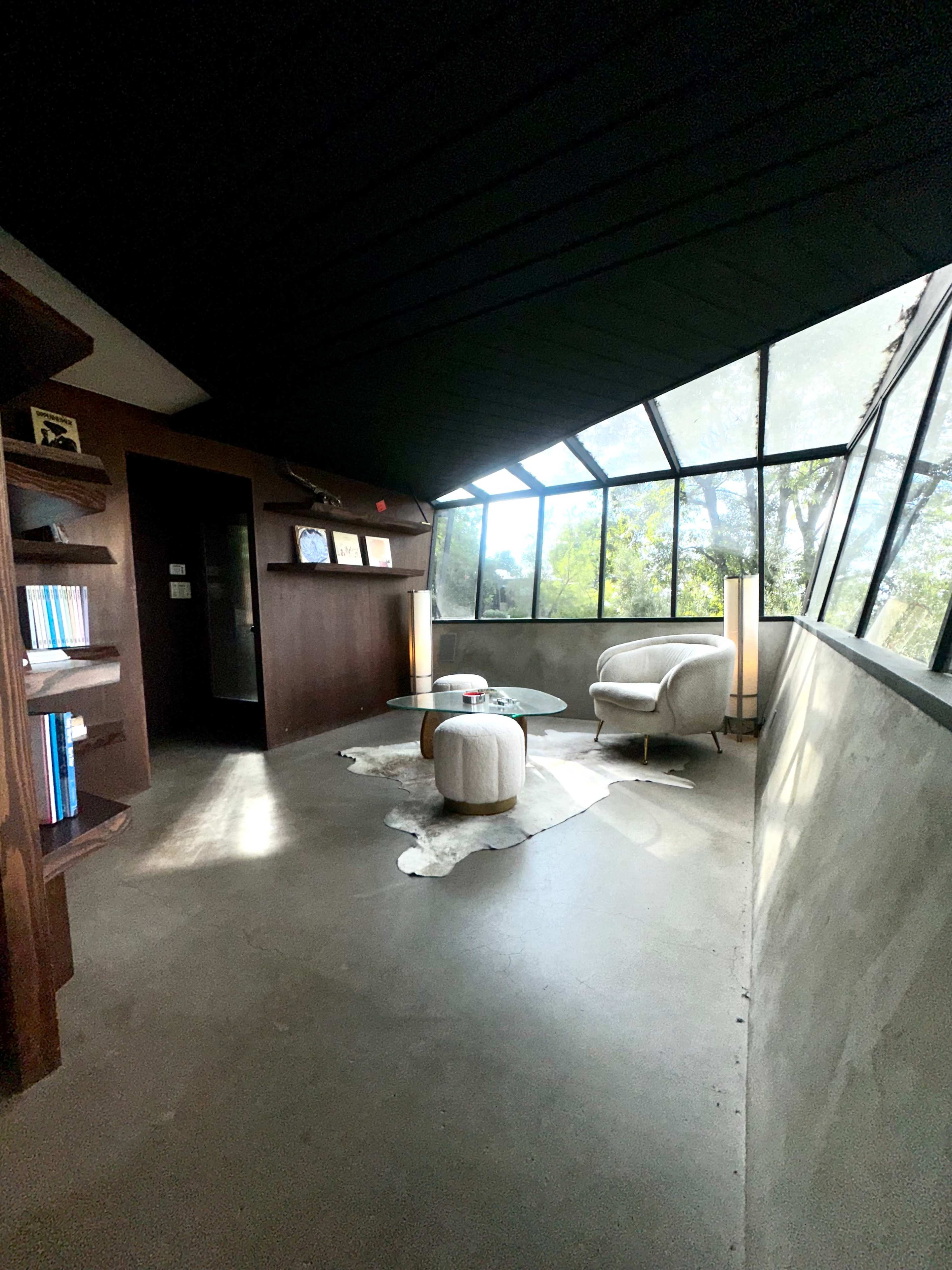 The image shows a modern interior space with large windows, a minimalist seating area, and a concrete floor.