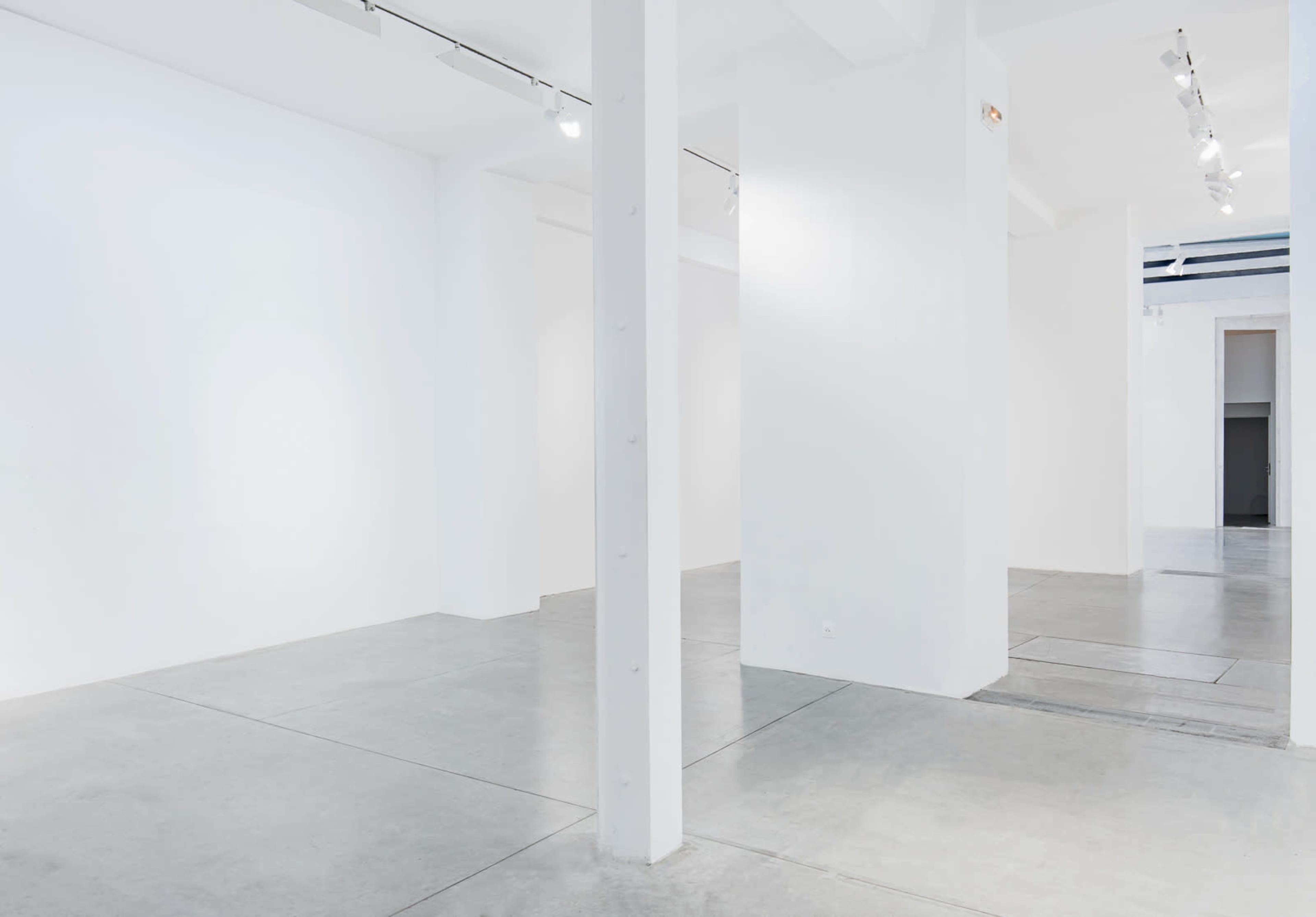 The image shows a spacious, empty art gallery with white walls and concrete flooring.