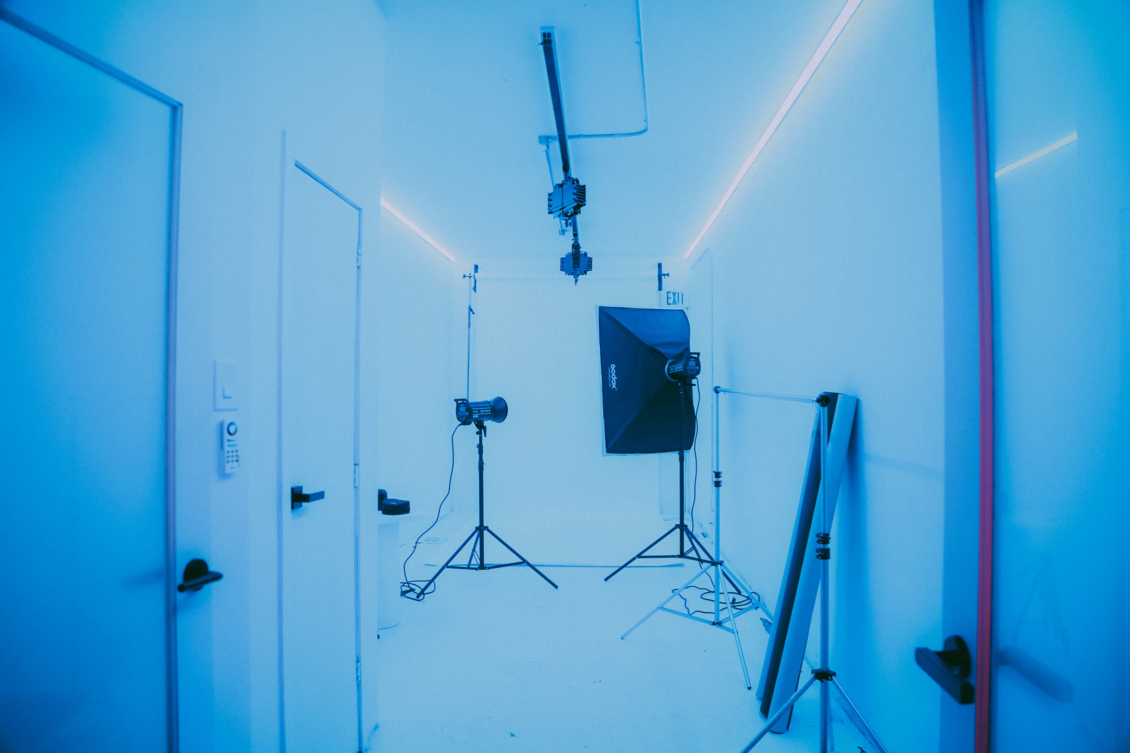 A well-lit studio room with blue walls, featuring backdrop supports, lighting equipment, and two doors.